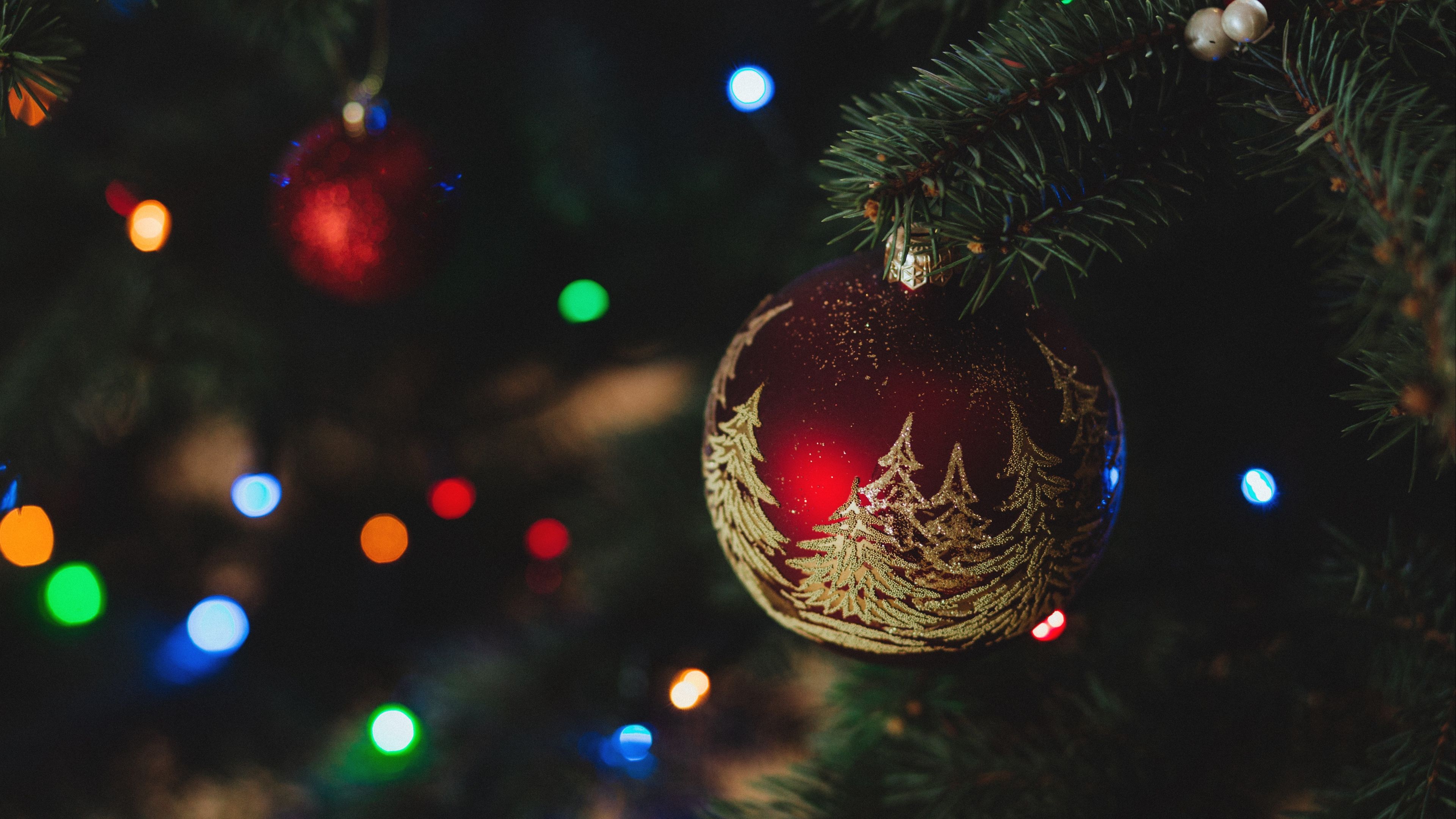 Close-up of a burgundy Christmas ornament with gold trees on a Christmas tree with colorful bokeh lights