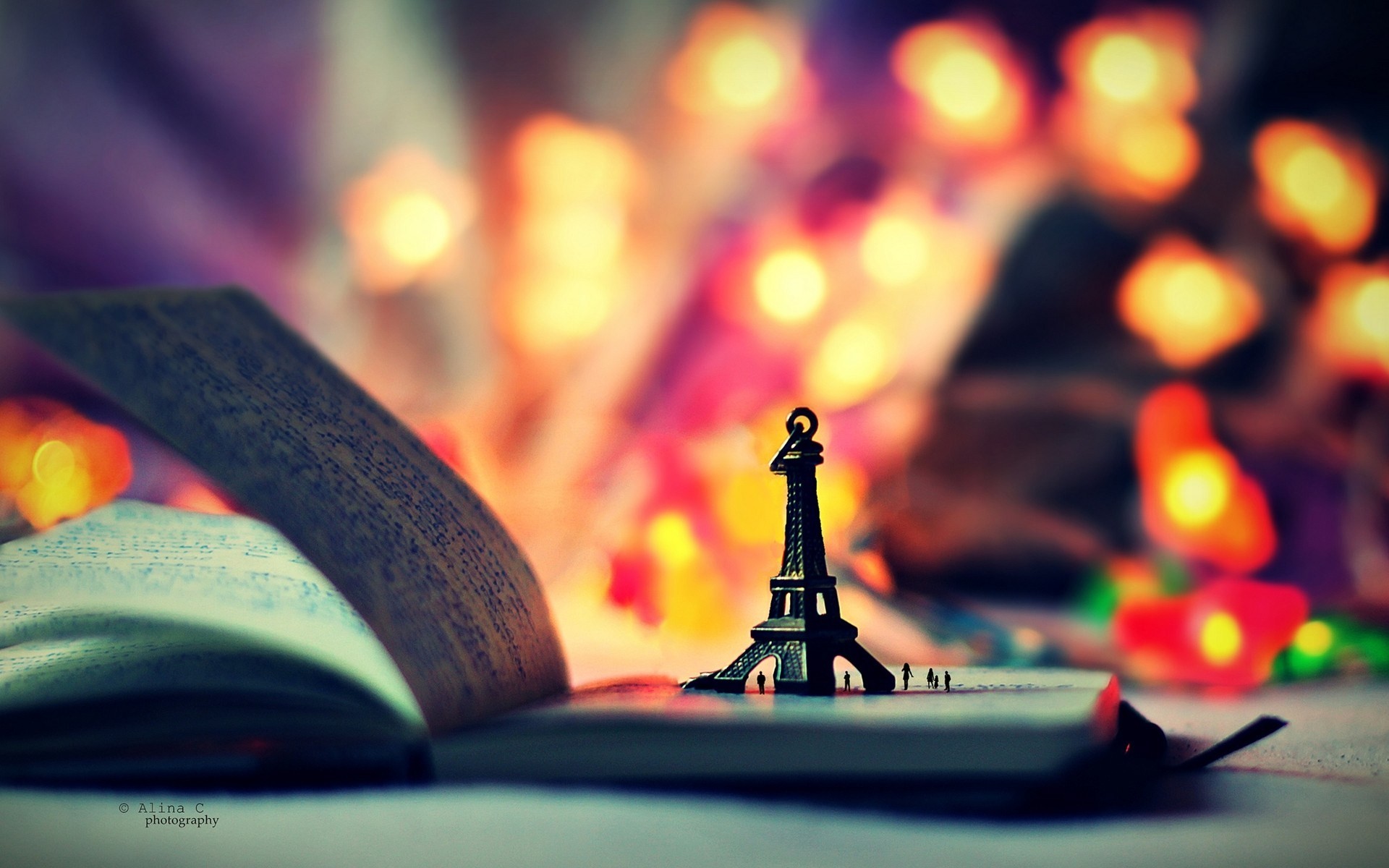 A miniature Eiffel Tower stands on a notebook against a backdrop of blurred fairy lights, evoking a whimsical and dreamy atmosphere