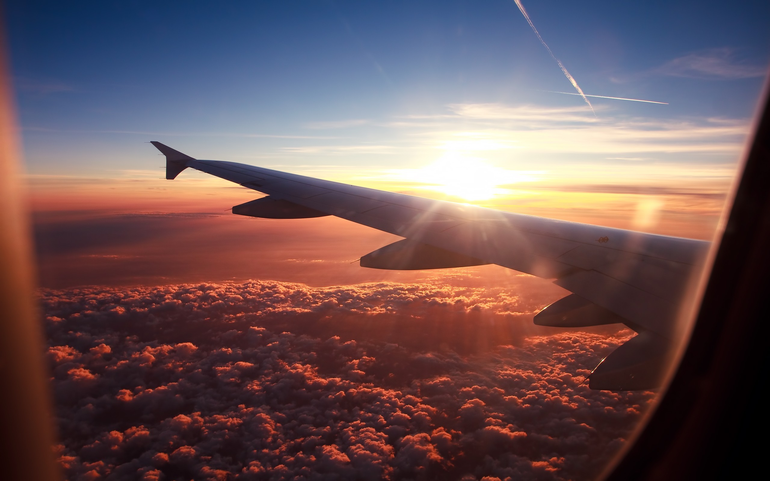 Airplane wing soaring above a breathtaking sunset, with a view of clouds from the window