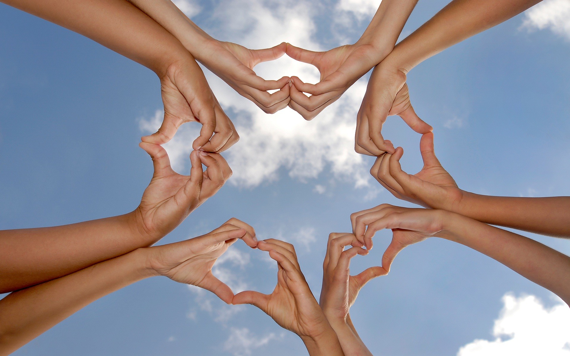 Multiple hands forming heart shapes against a blue sky, symbolizing friendship and unity