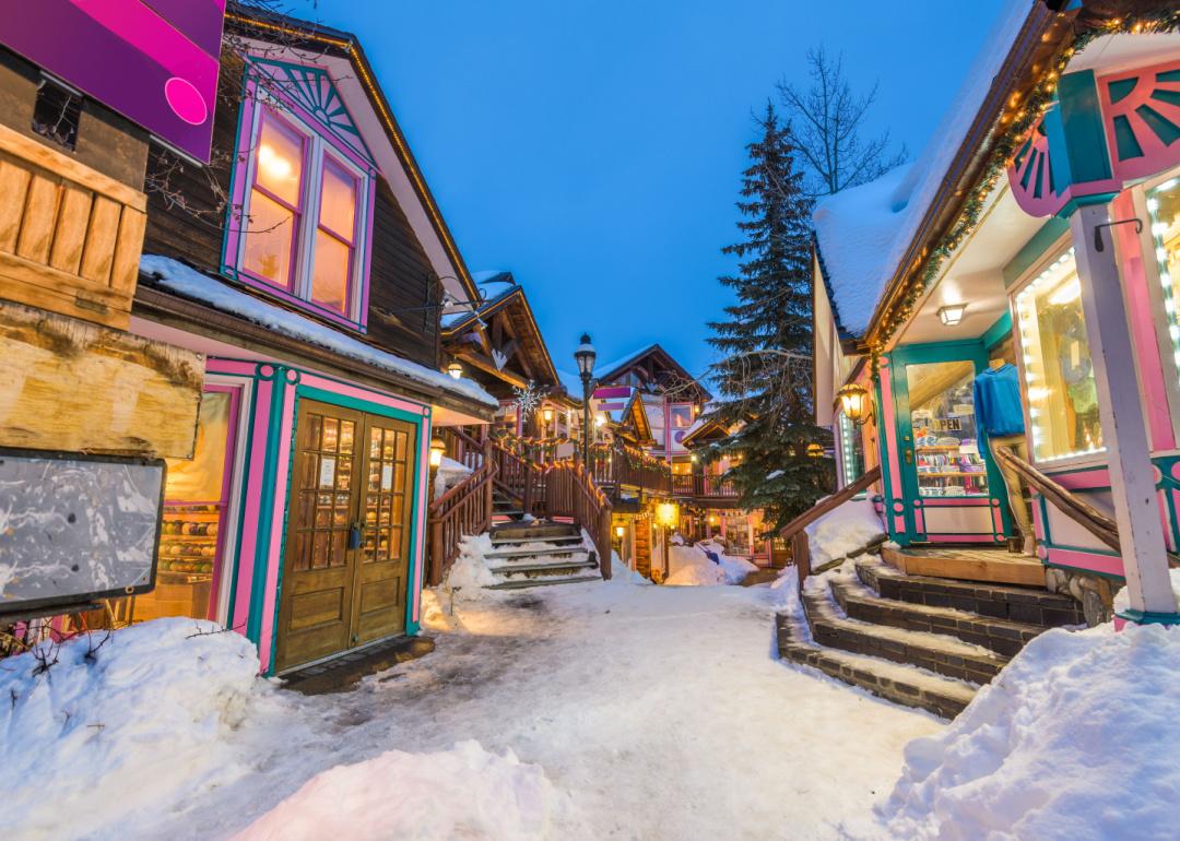 A charming snow-covered street in a cozy city at dusk, lined with colorful buildings and glowing lights