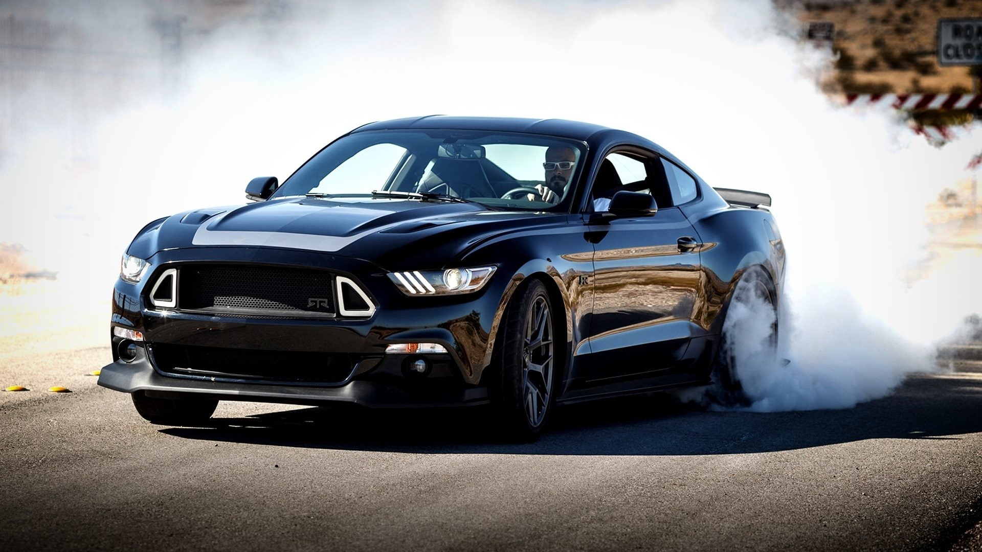 Black Ford Mustang drifting on a closed road, emitting smoke from its tires
