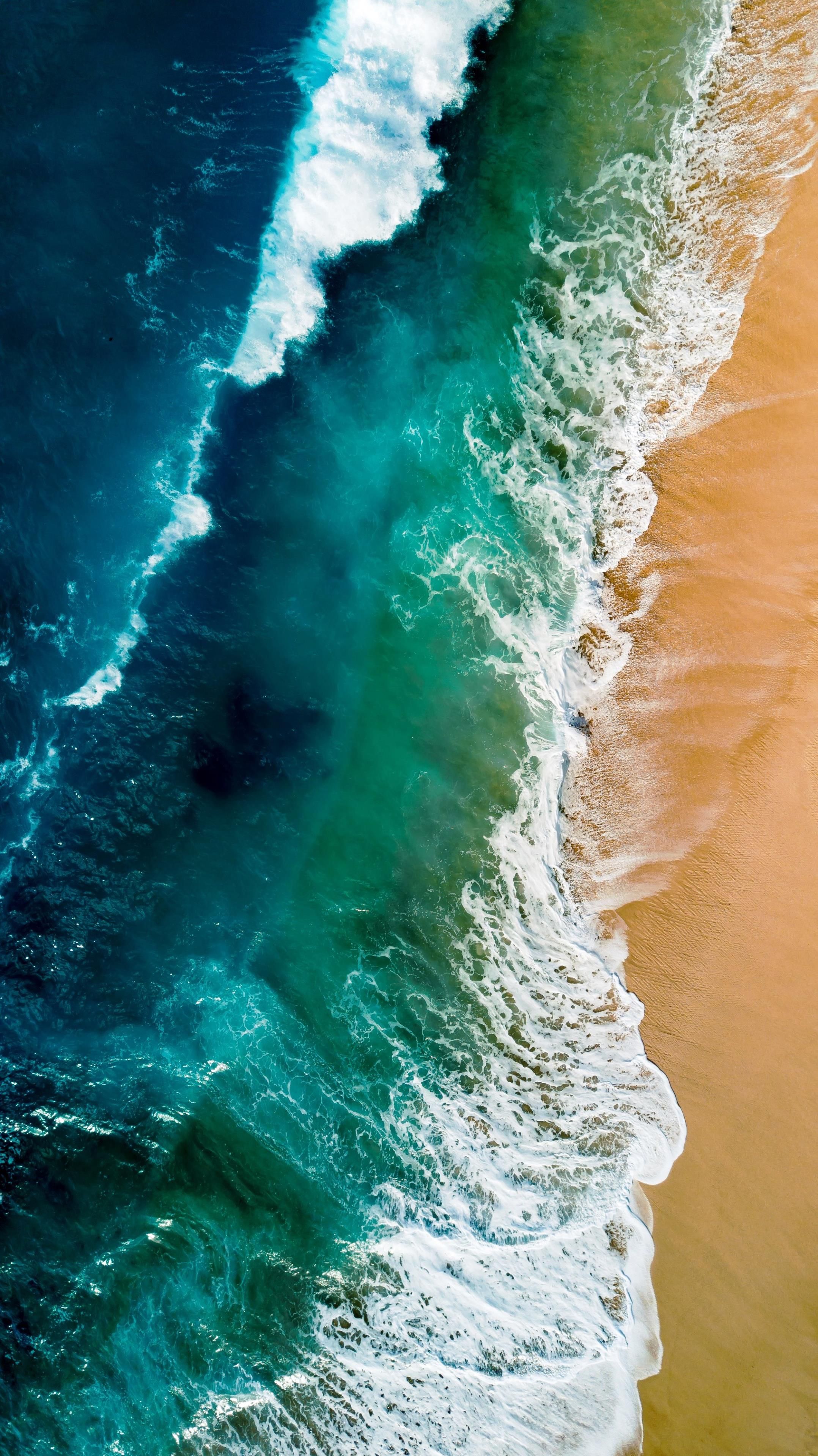 Aerial view of turquoise ocean waves crashing on a golden sandy beach, creating a stunning contrast between the vibrant blue water and the warm tones of the sand