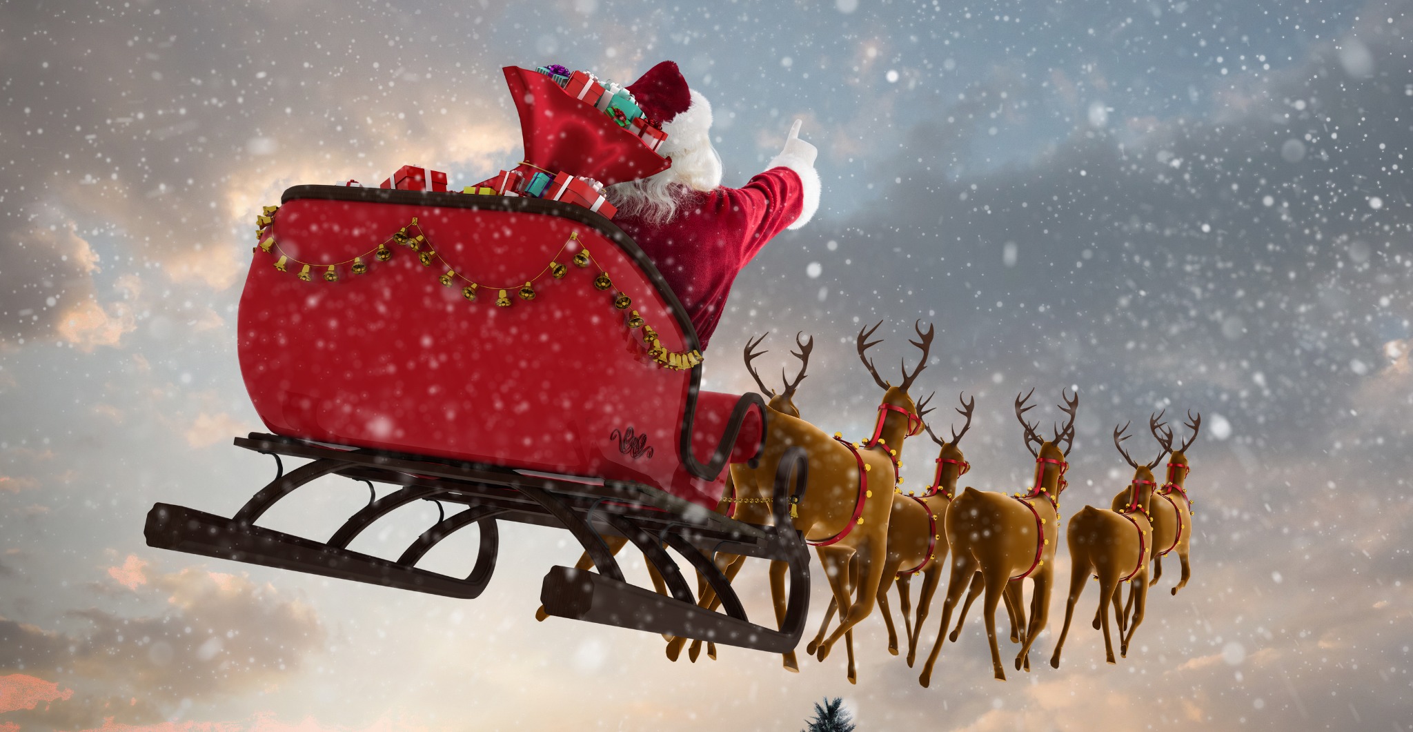 Santa Claus flying his sleigh with reindeer through a snowy sky, delivering presents for Christmas. A classic festive image for wallpapers
