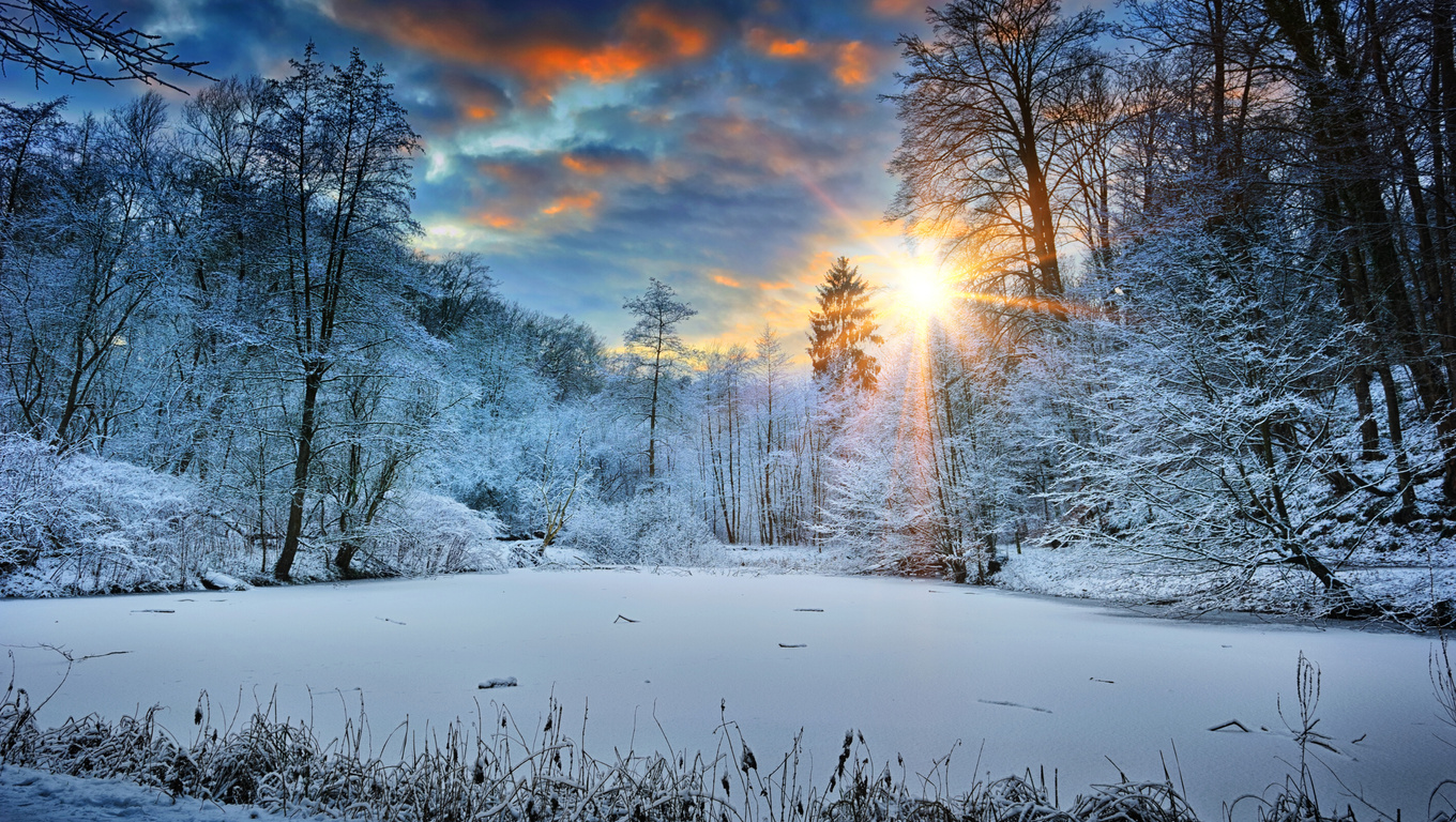 A breathtaking 4k winter wallpaper featuring a serene frozen lake surrounded by snow-covered trees and a beautiful sunset in the background