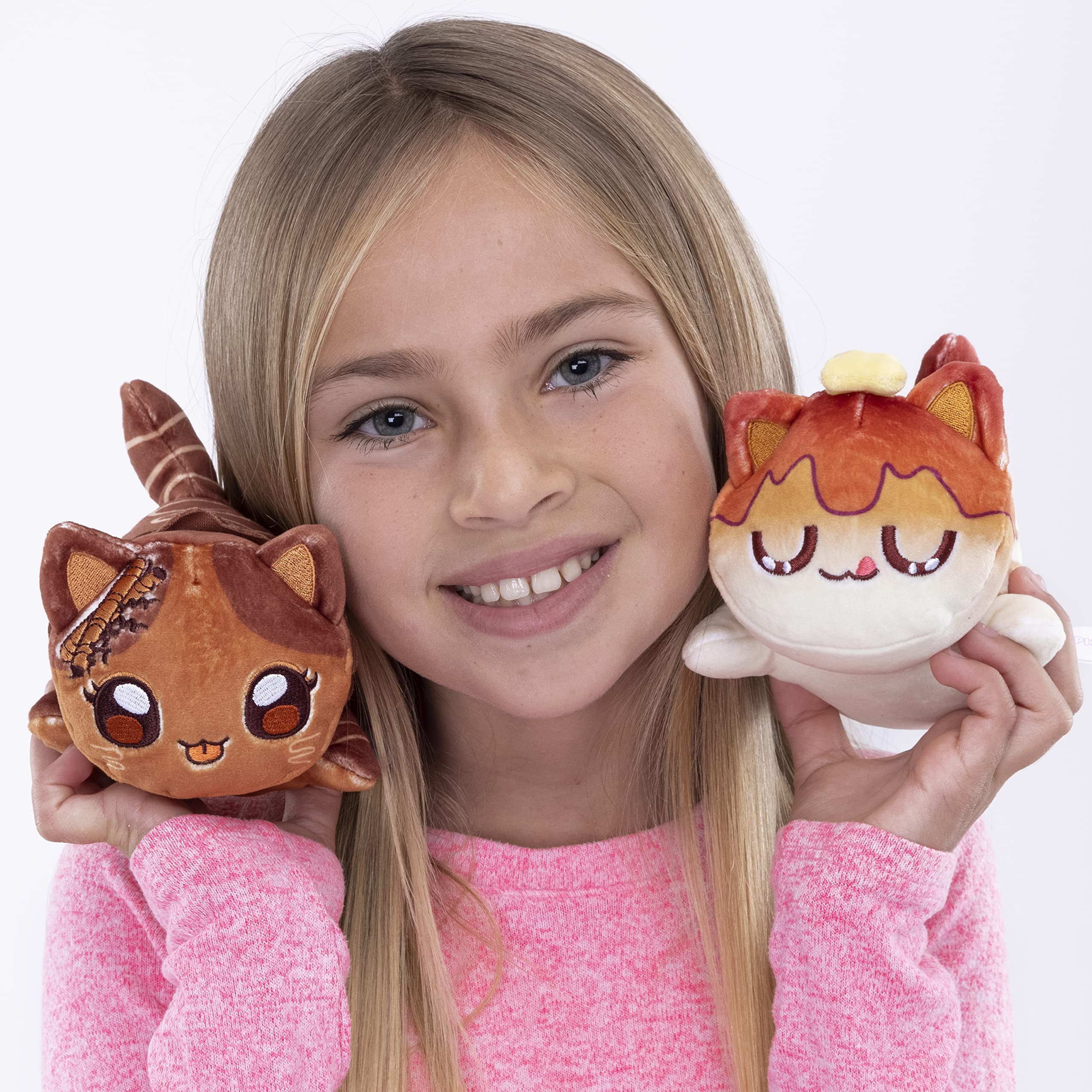 A young girl smiles while holding two adorable plush toys, a cat and another cat-like creature