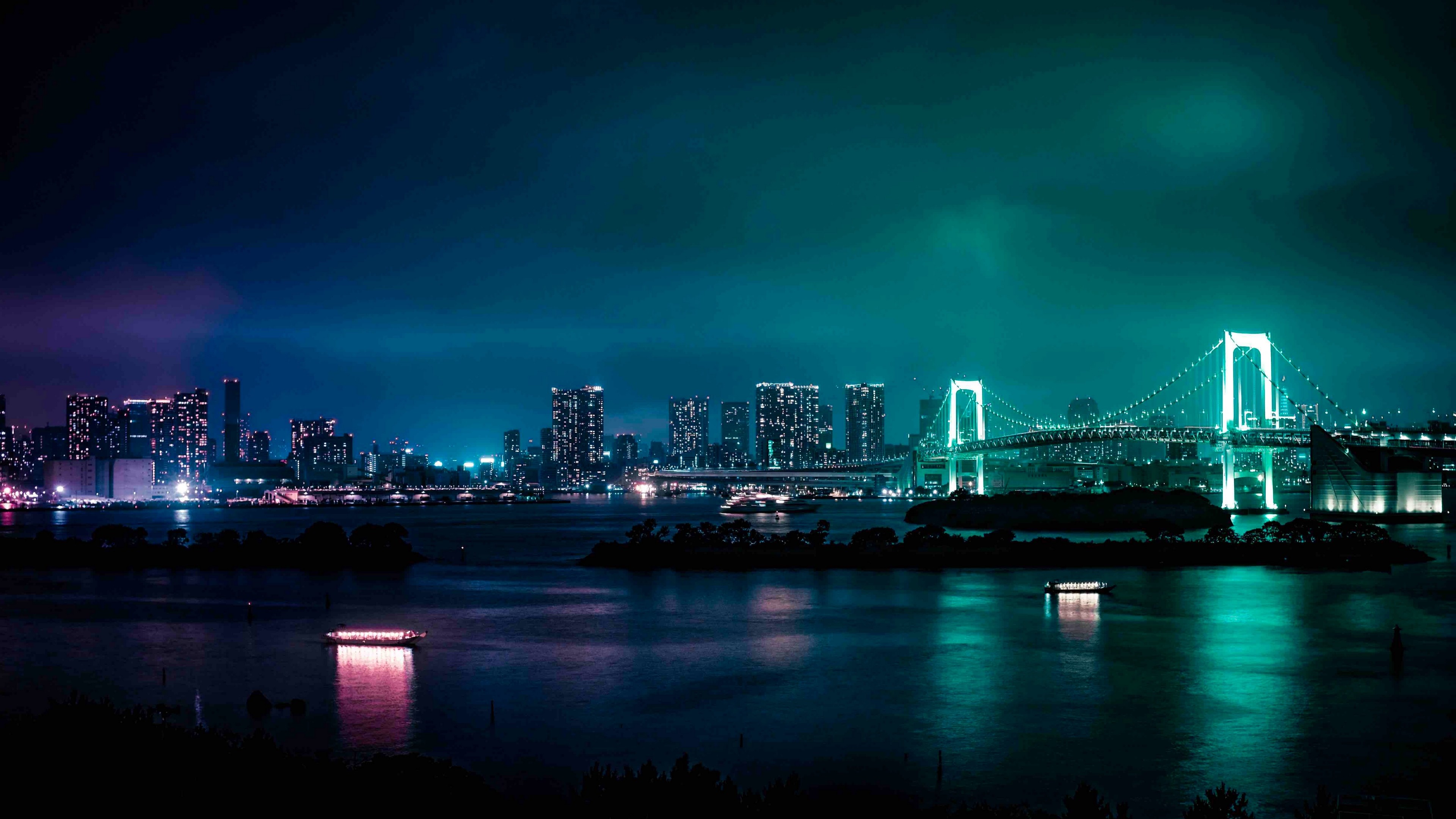 A stunning 4K wallpaper of the Rainbow Bridge in Tokyo, Japan at night, illuminated in vibrant teal against a backdrop of a dark cityscape