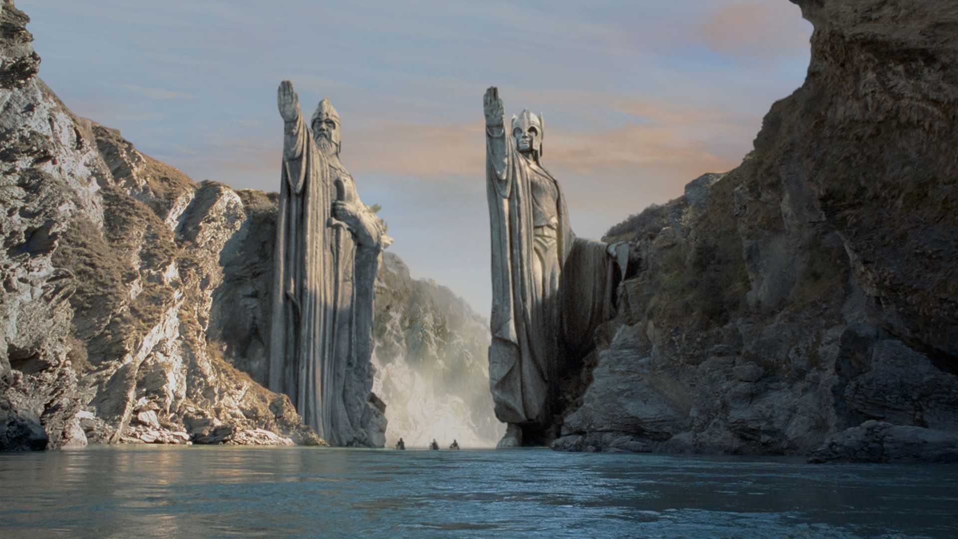 Two colossal statues guard the entrance to a river in a dramatic scene from The Lord of the Rings
