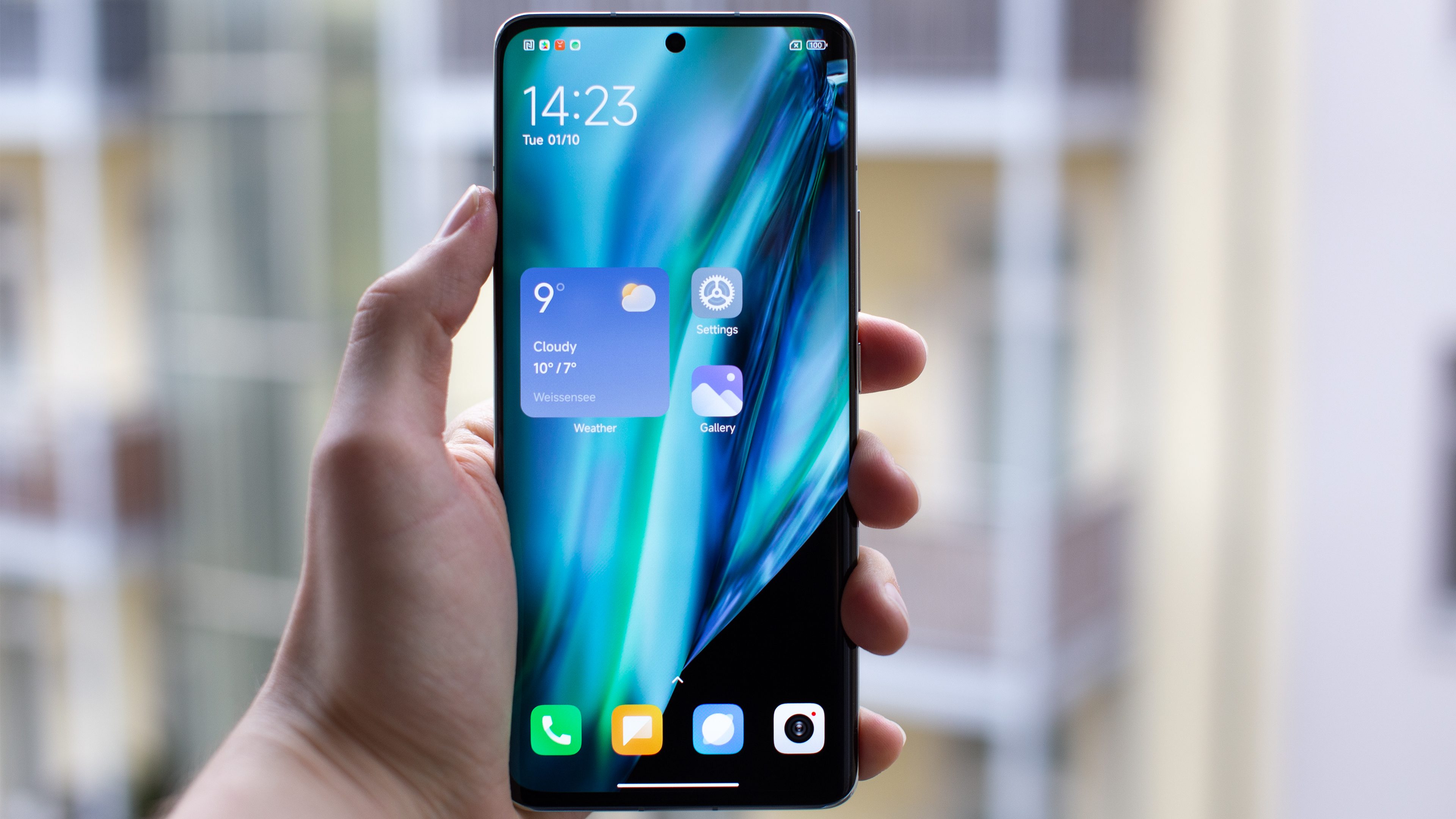 A hand holding the Xiaomi 14 Pro, displaying the phone's home screen with its default wallpaper