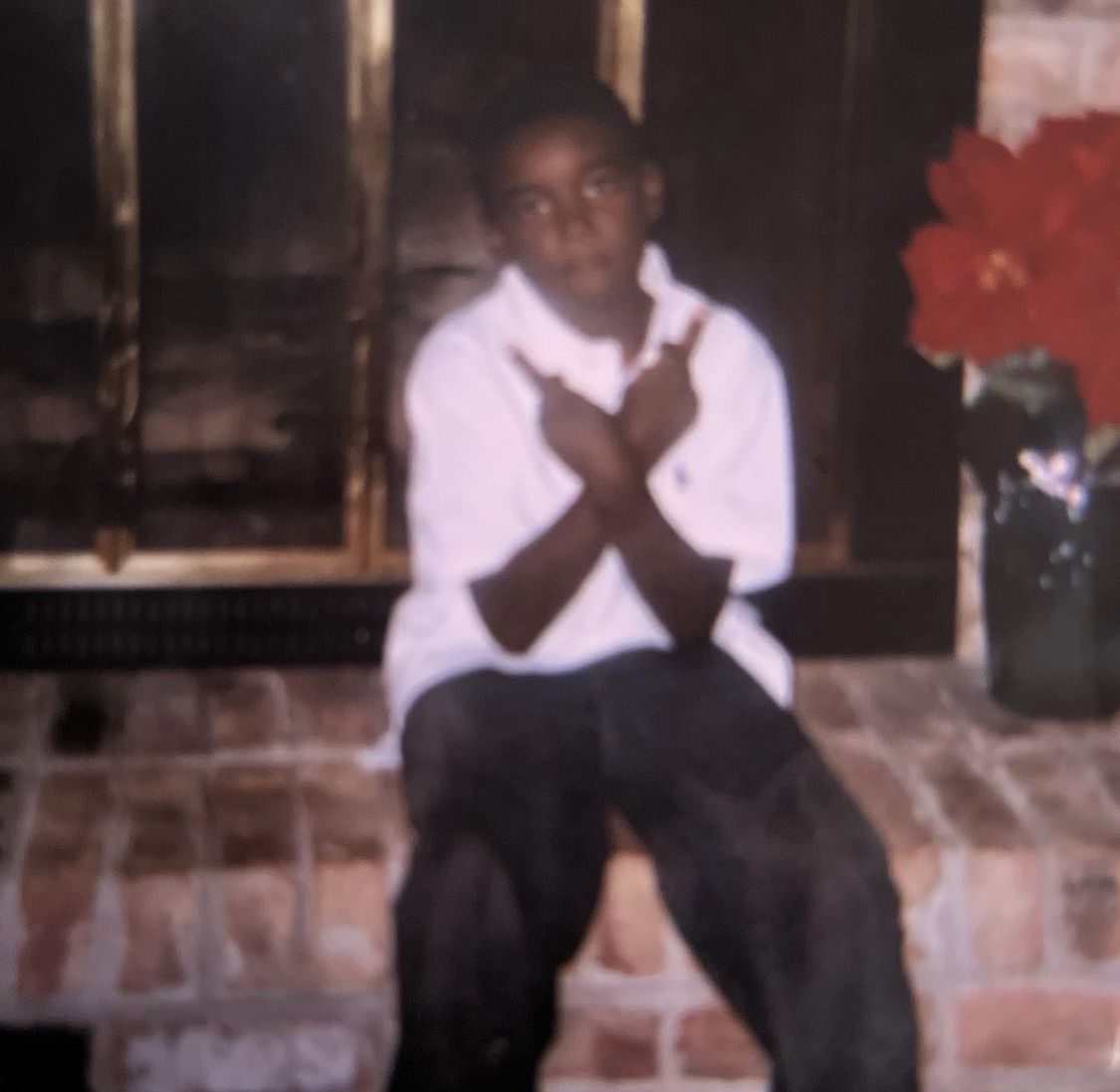 A blurry photo of a young child sitting in front of a fireplace, making a gesture with their crossed arms