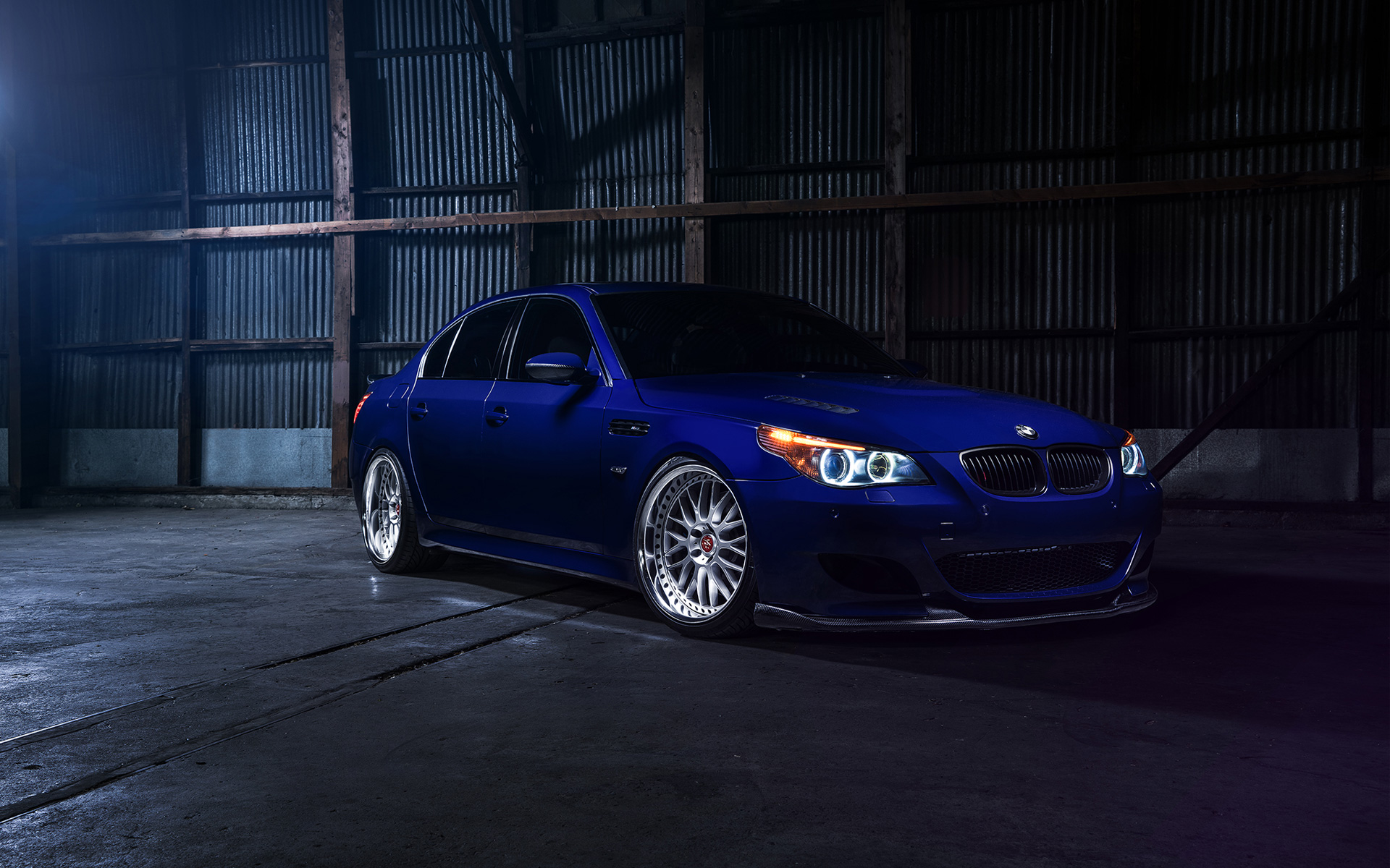 A vibrant blue BMW M5 parked in a dimly lit industrial warehouse, showcasing its sporty design and powerful presence