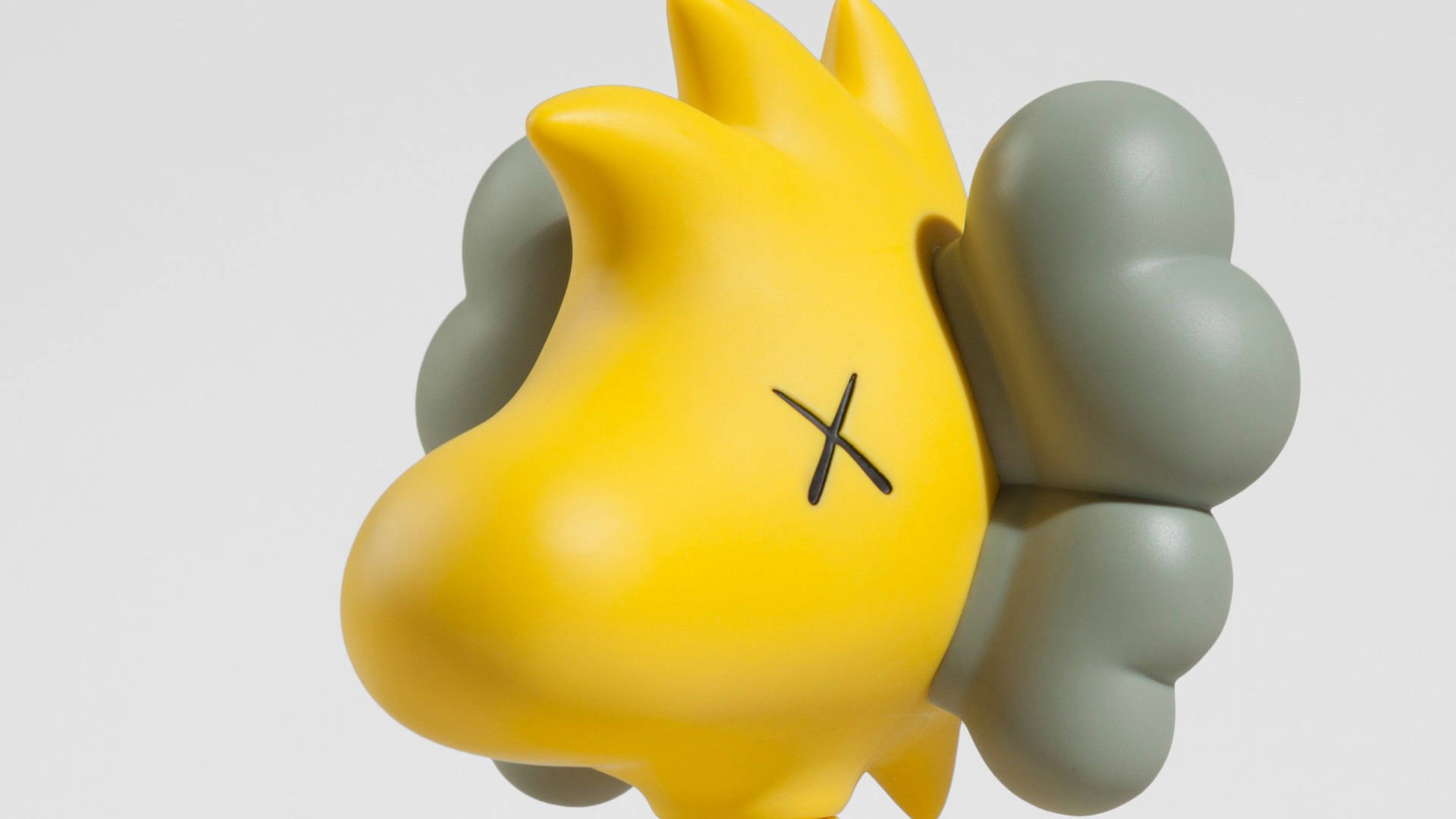 Close-up of a Kaws Companion figure featuring a Snoopy-inspired design in yellow and grey, against a light grey background