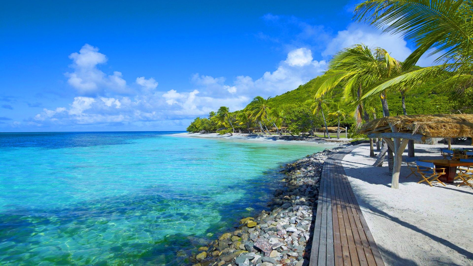 Tropical island beach with crystal-clear turquoise water, palm trees, and a wooden walkway