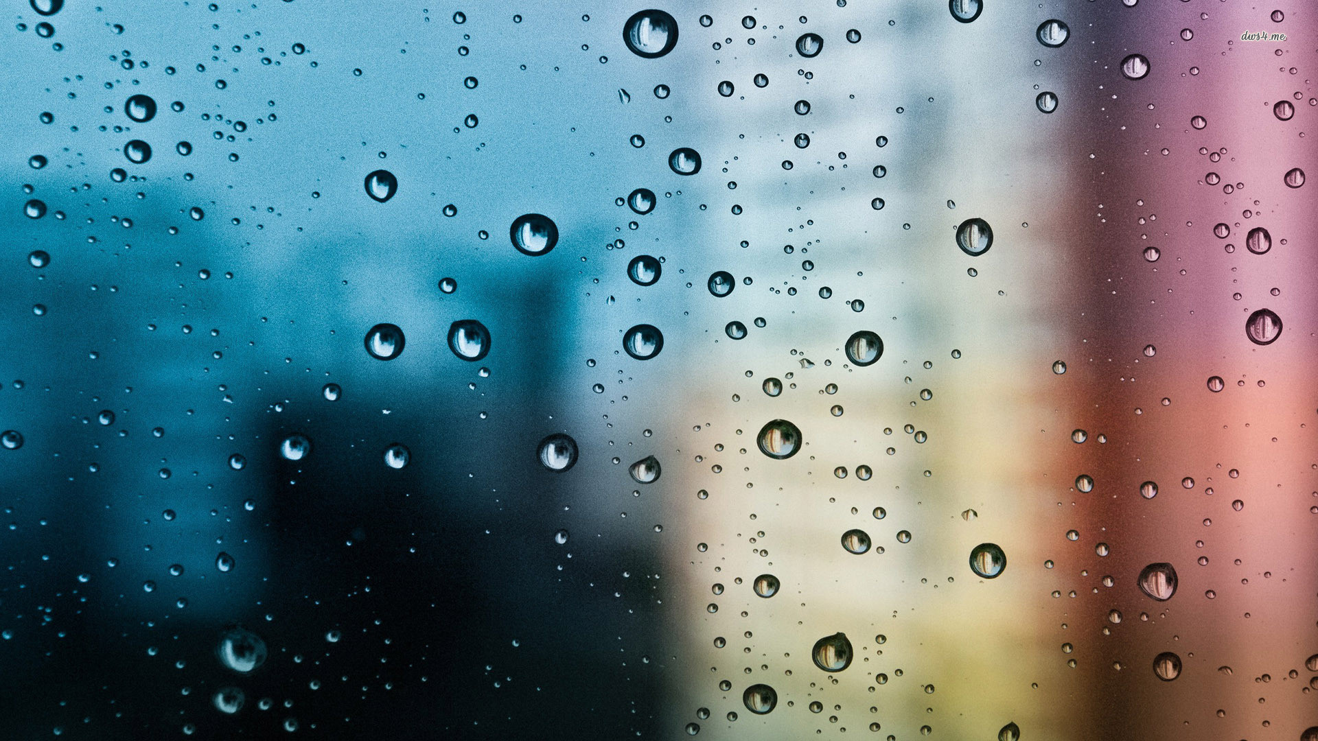 Close-up of raindrops on a window, blurring the colorful background of buildings