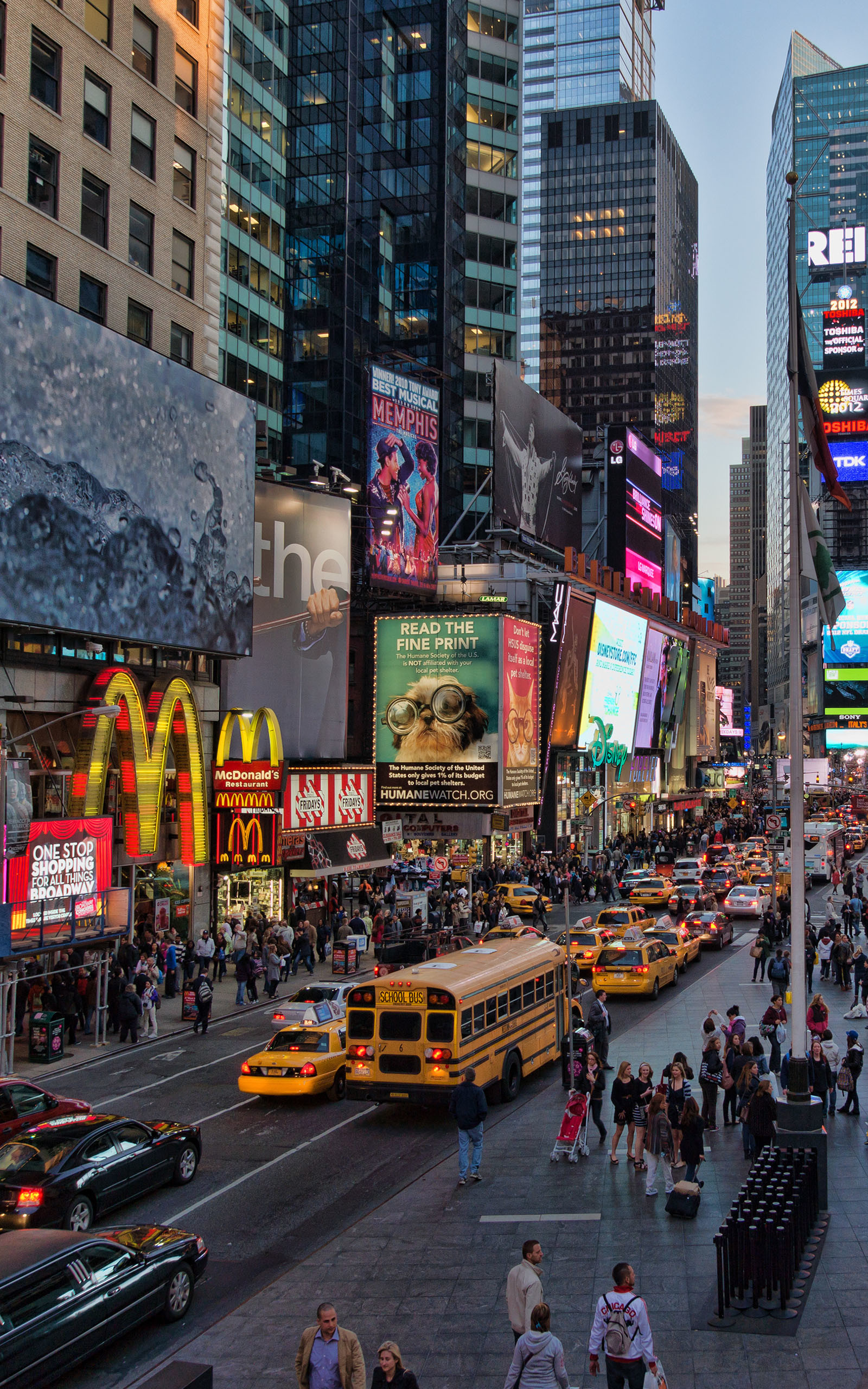 A vibrant street view of New York City's Times Square at dusk, featuring iconic billboards, bustling crowds, and yellow taxis