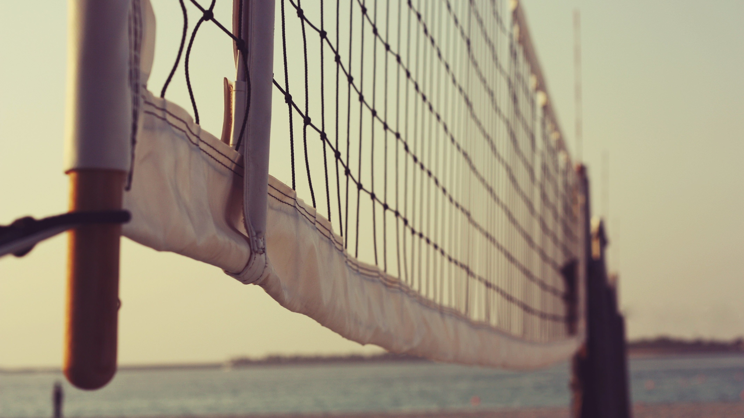 Close-up of a beach volleyball net at sunset, with the ocean and beach blurred in the background
