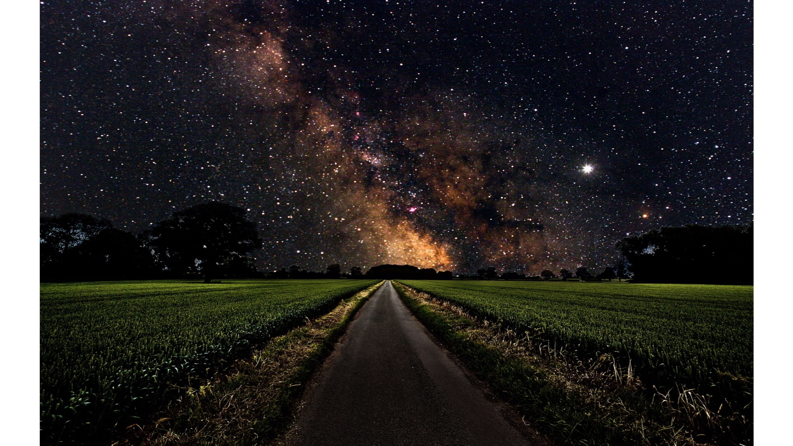 A mesmerizing night scene featuring a dark road leading through a green field towards a backdrop of the Milky Way galaxy, illuminating the night sky with countless stars