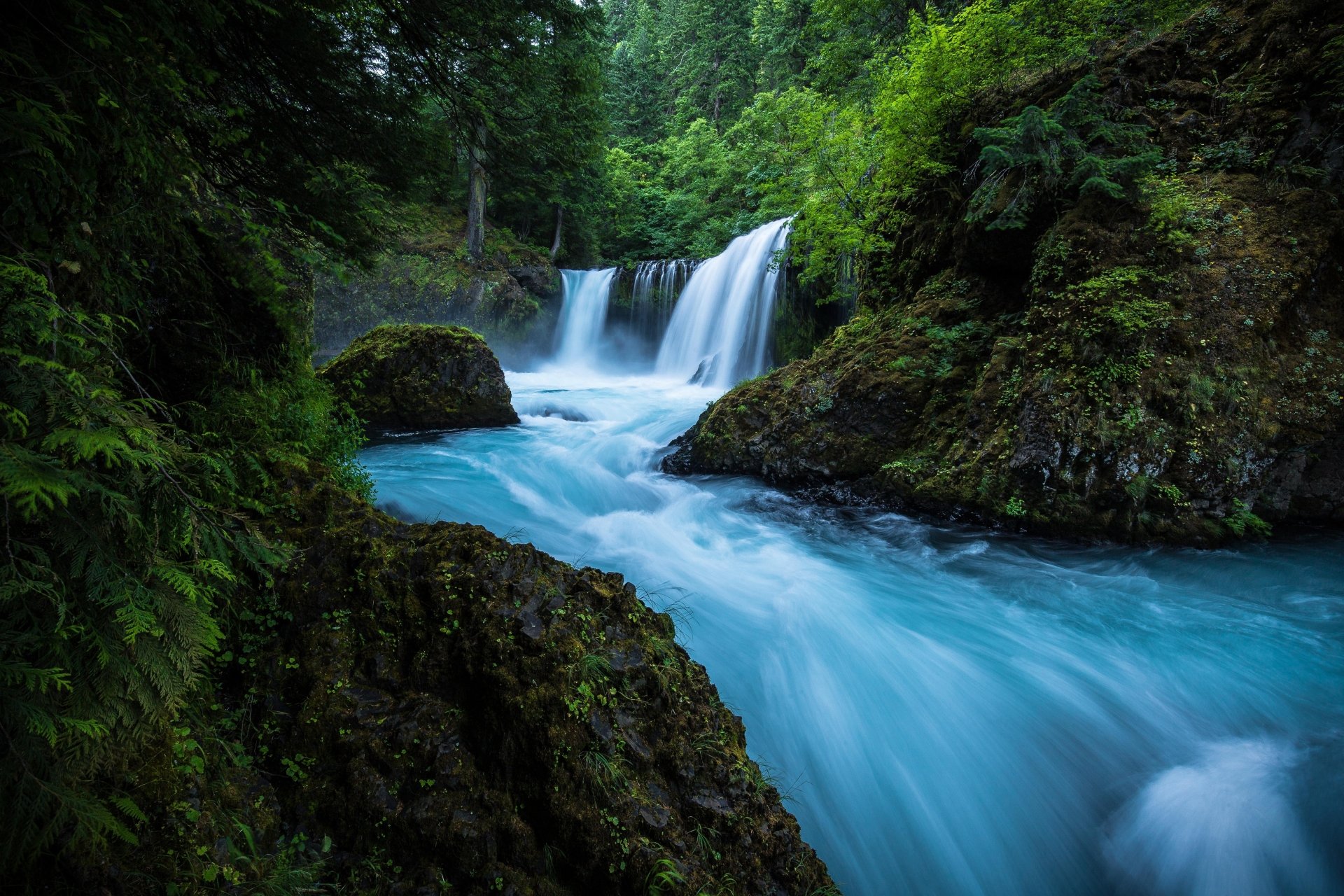 A breathtaking 4k wallpaper of a cascading waterfall flowing into a vibrant turquoise river, surrounded by lush green forest