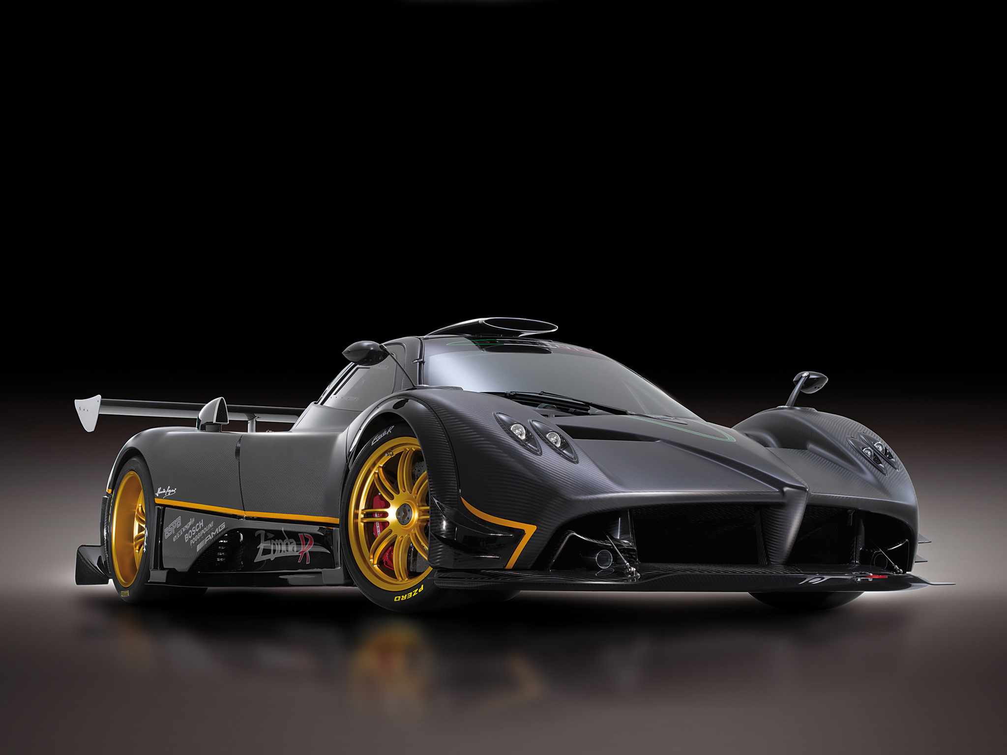 A sleek, dark gray Pagani Zonda R supercar with gold accents, showcased against a black background. Its aerodynamic design and low profile are highlighted, emphasizing its high-performance nature