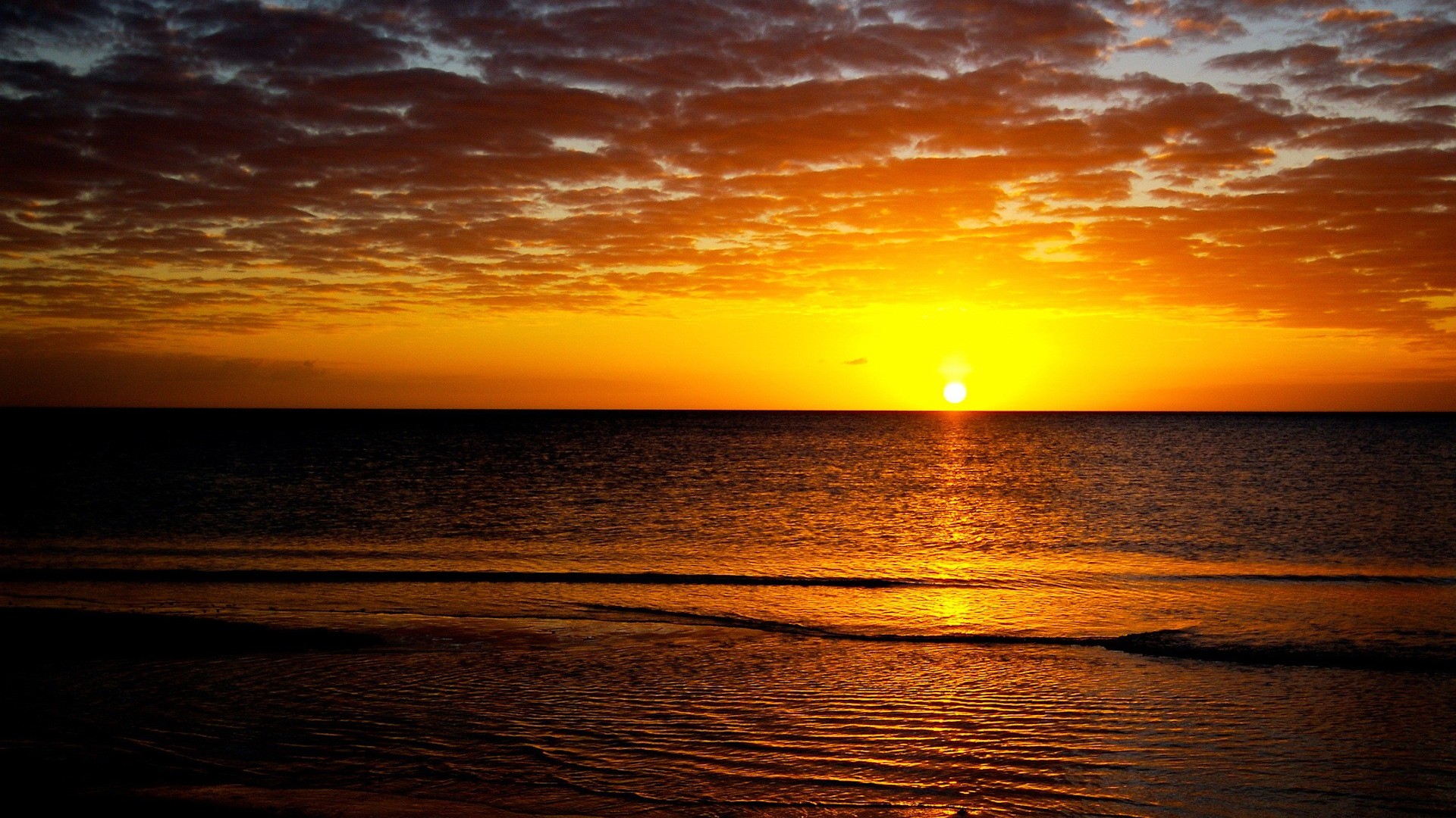 A breathtaking sunset over a tranquil ocean, with vibrant orange and yellow hues painting the sky and reflecting on the gentle waves