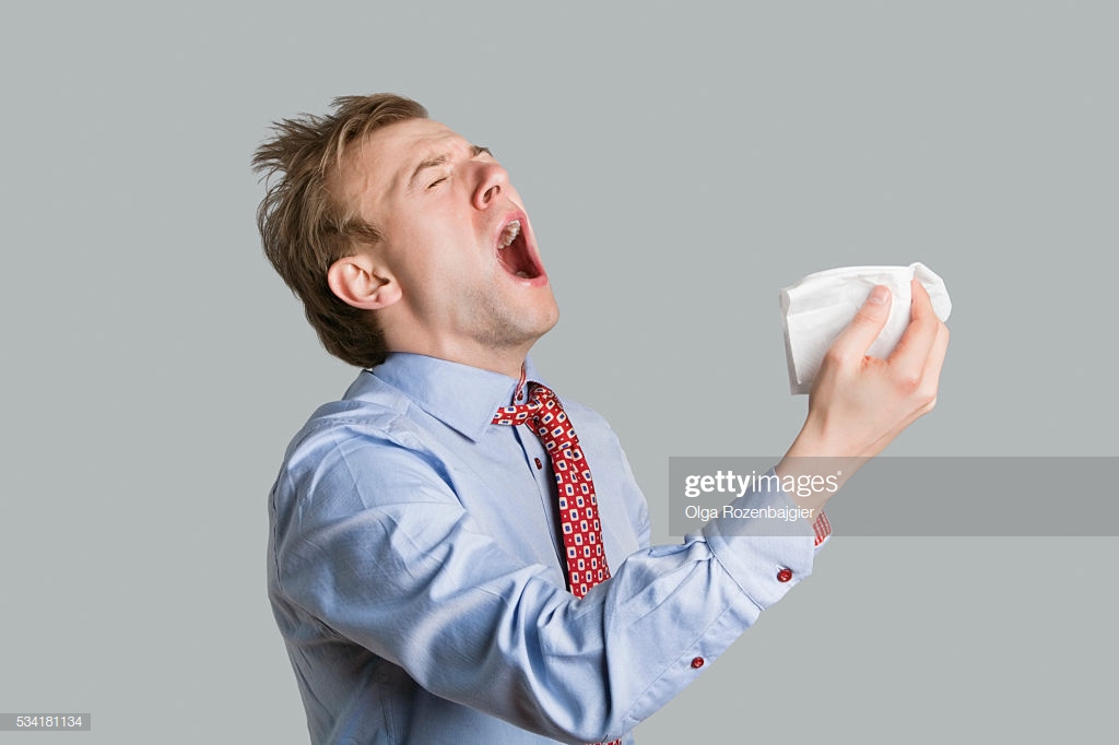 Young Man Sneezing With Open Mouth And Handkerchief Over Colored