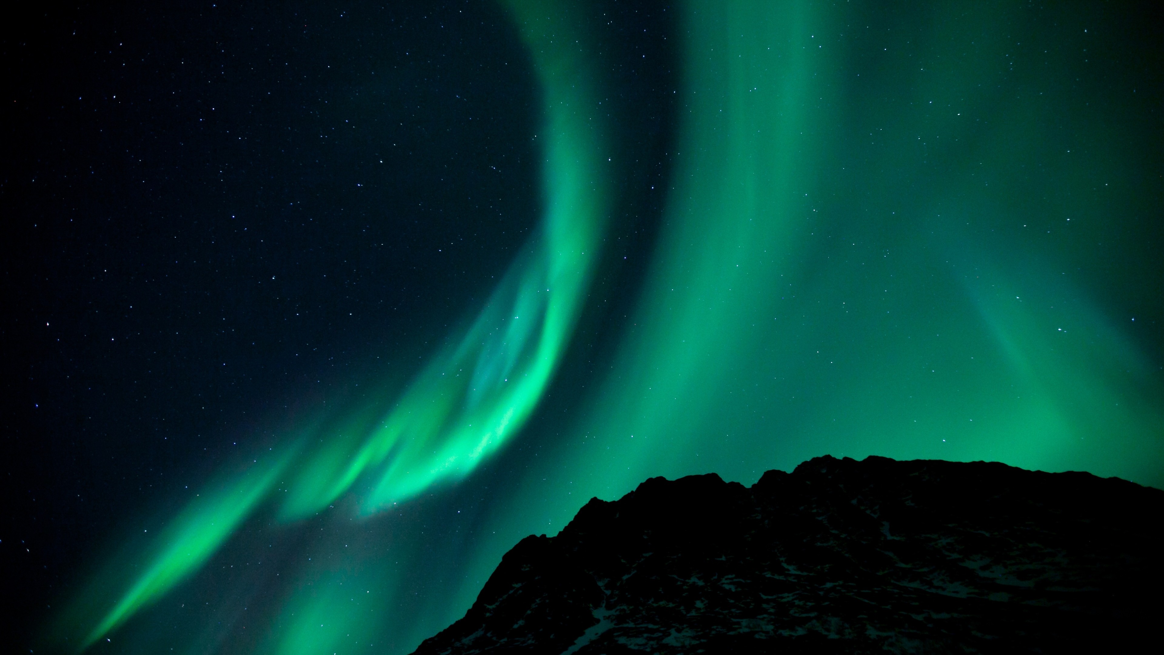Vivid green aurora borealis dancing across a starry night sky, illuminating the silhouette of a mountain range below