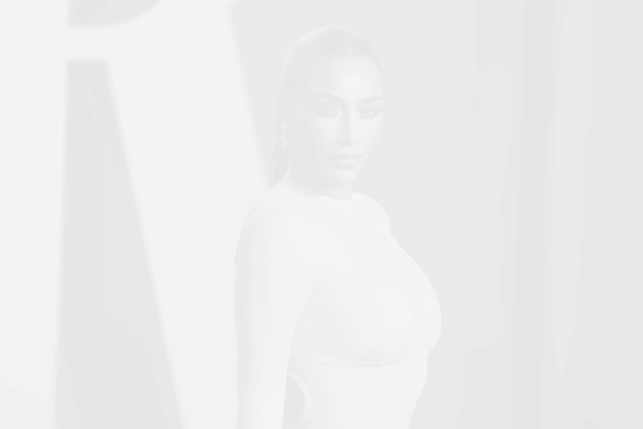 A blurry image of a person, potentially Kim Kardashian, standing against a white background with light and shadow patterns