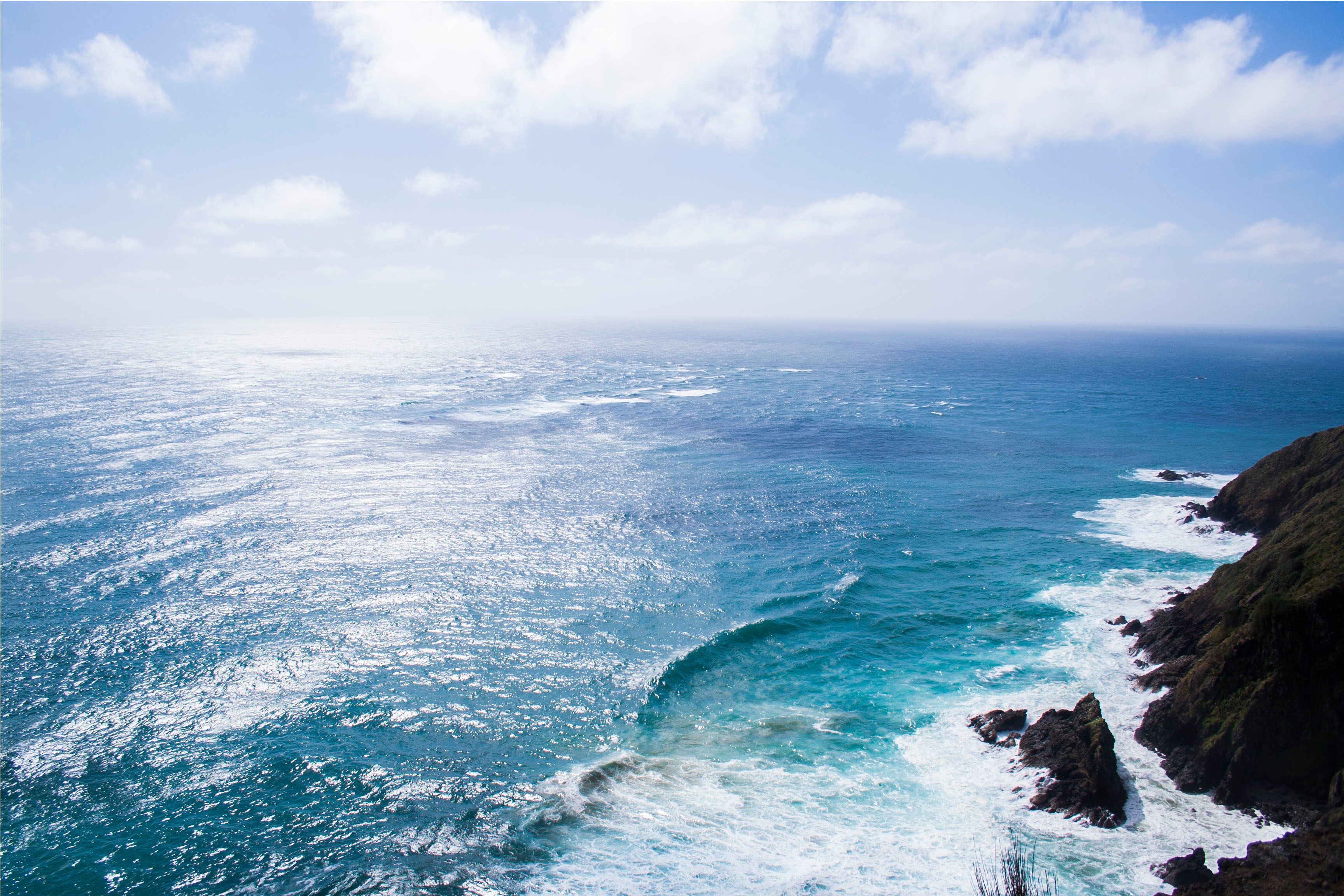 Vast ocean view with waves crashing against a rocky coastline under a bright blue sky
