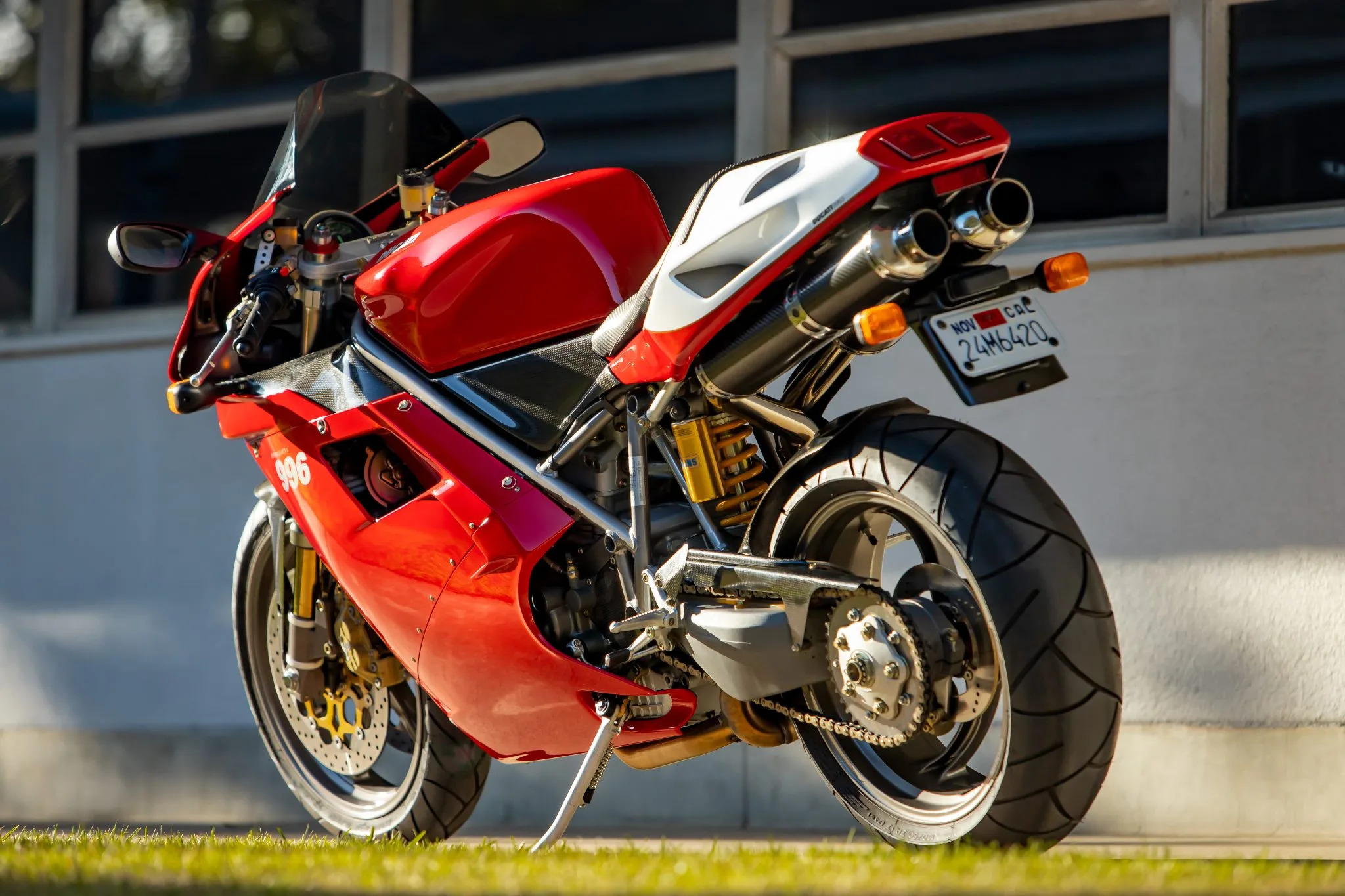 A Ducati 996 motorcycle parked outdoors, showcasing its red and white bodywork, dual exhaust, and gold suspension
