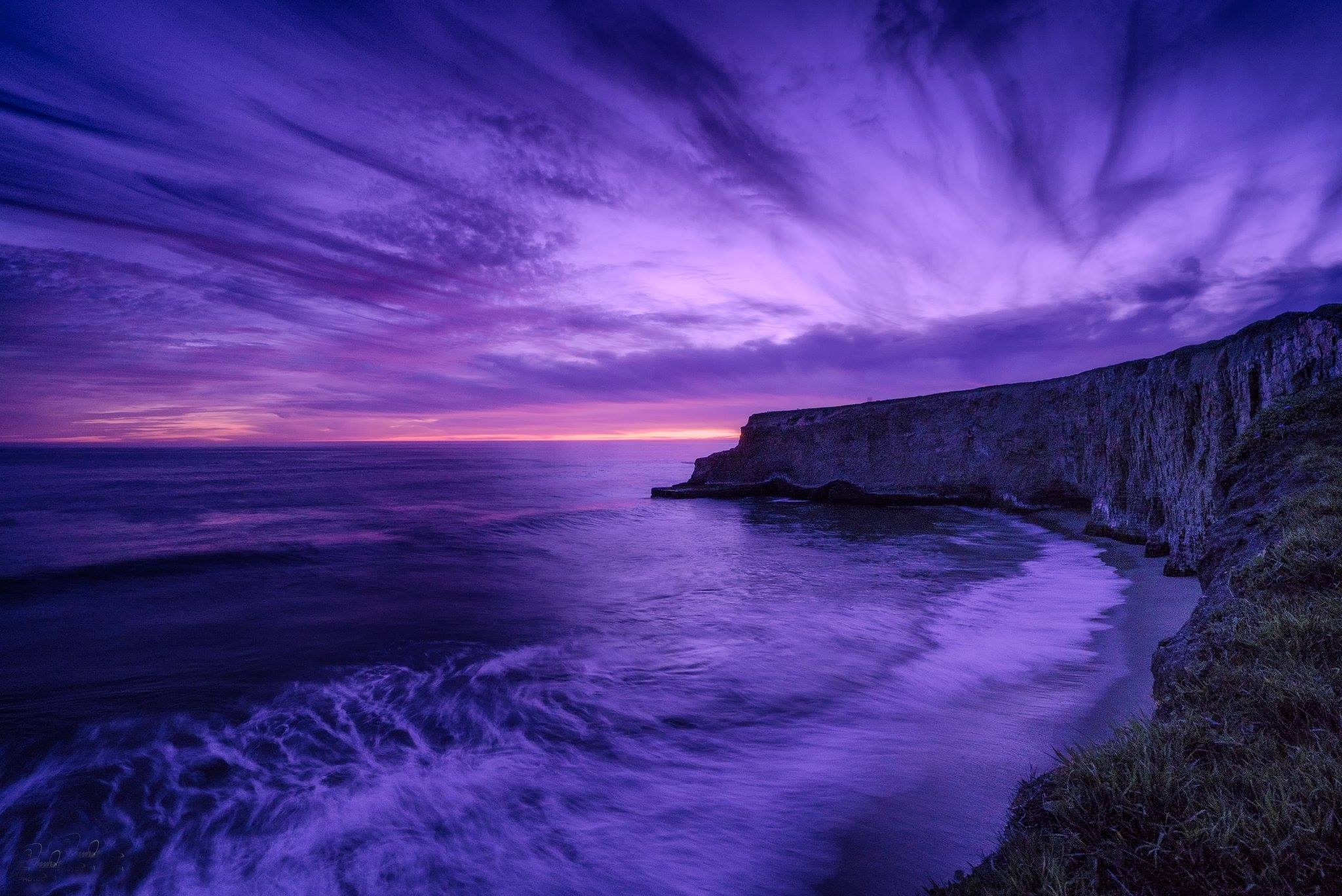 Dramatic purple sunset over a rocky coastline with waves crashing on the shore