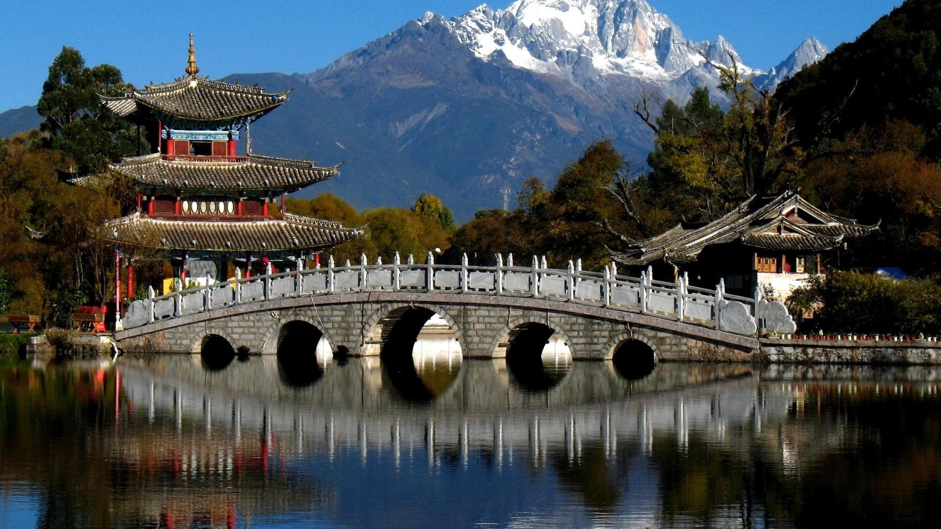 A picturesque scene of traditional Chinese architecture reflected in a serene lake, set against the backdrop of the Jade Dragon Snow Mountain in Lijiang, Yunnan, China