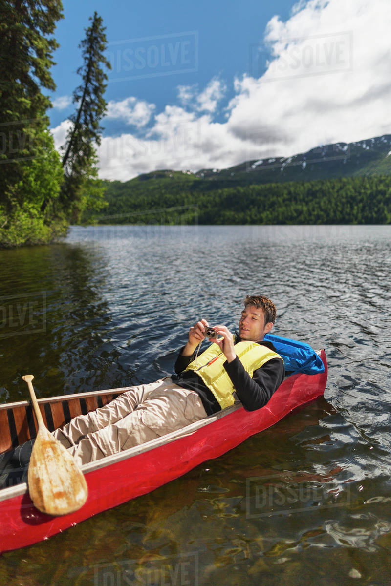 Man Reclined In Canoe And Checking His Camera On Byers Lake With