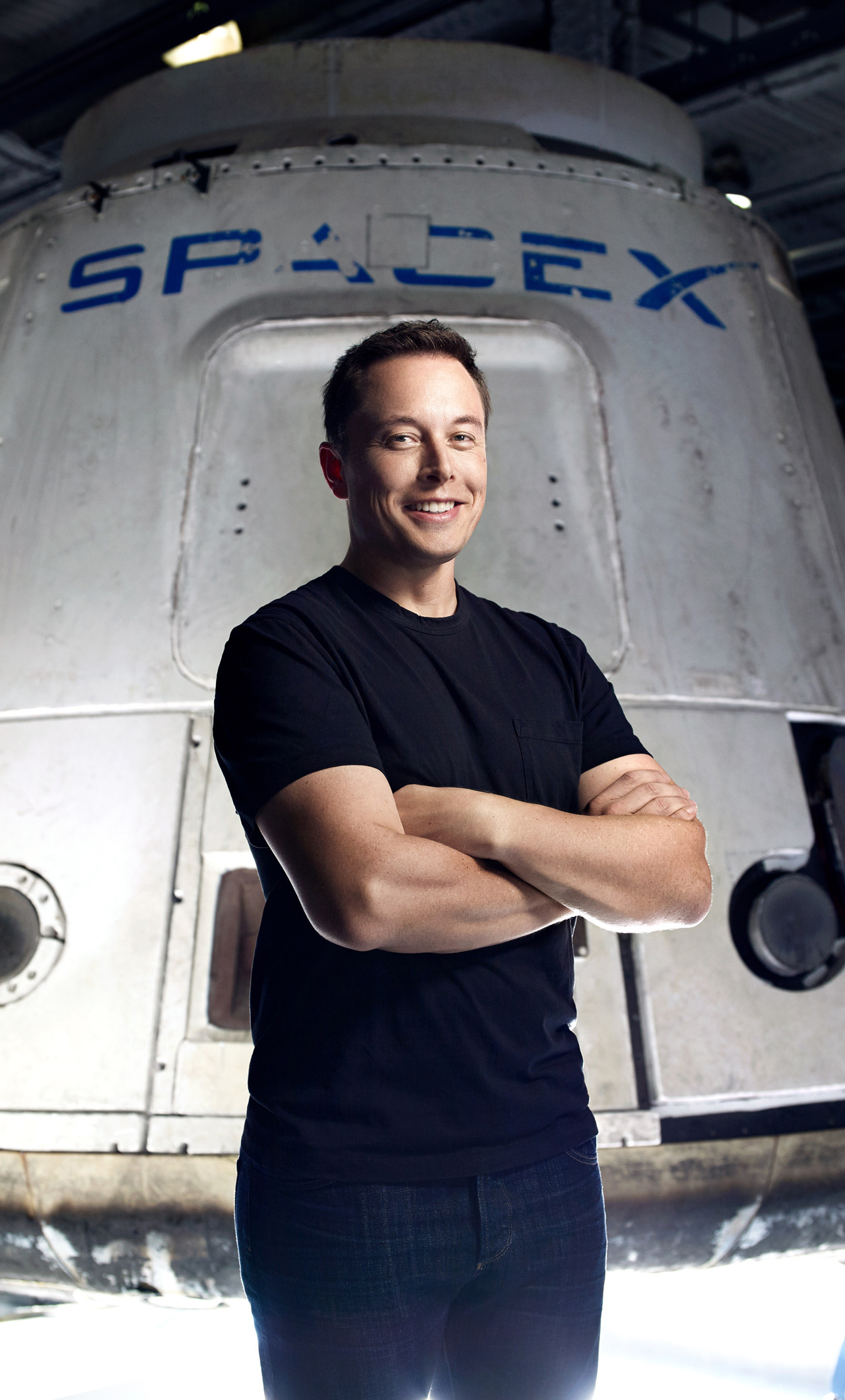 Elon Musk, CEO of SpaceX, stands with his arms crossed in front of a SpaceX spacecraft