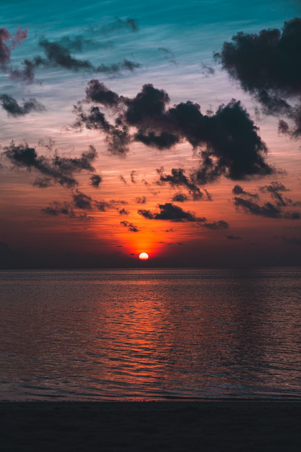 The Sun Is Setting Over Ocean On A Cloudy Day Photo