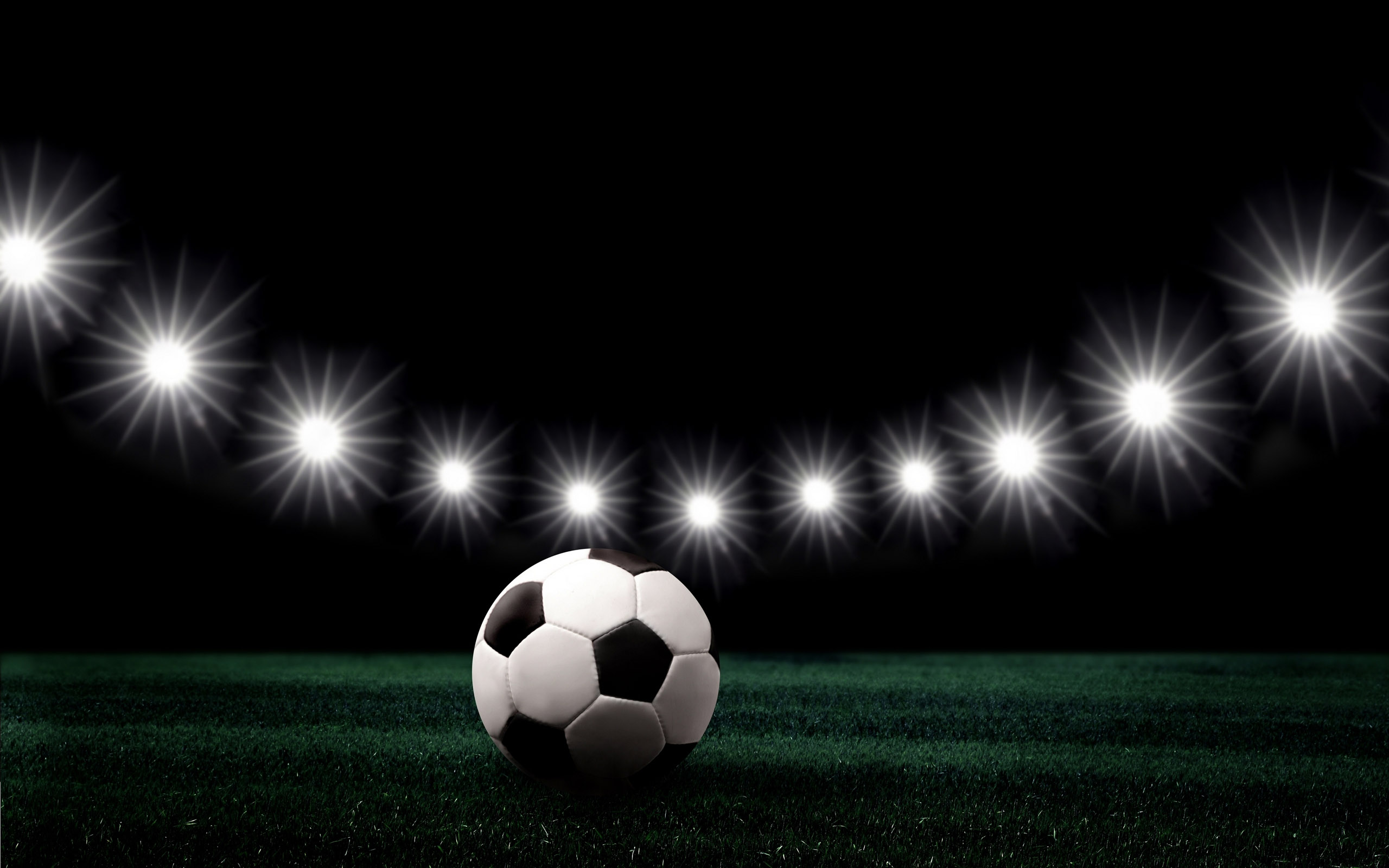 A classic black and white soccer ball sits on a lush green field under the bright lights of a stadium at night
