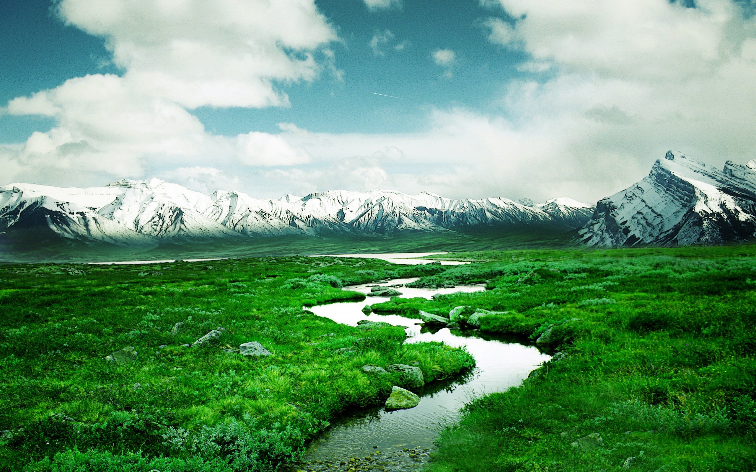 A breathtaking landscape with a meandering stream, lush green fields, and snow-capped mountains under a vibrant sky