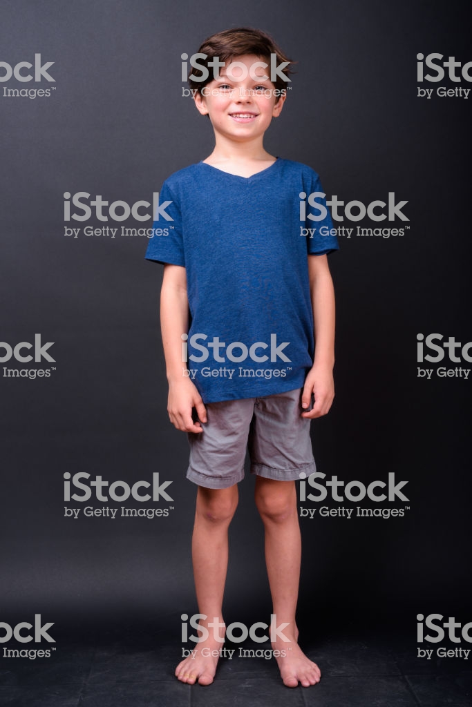 Portrait Of Cute Boy Standing Barefoot Against Black Background