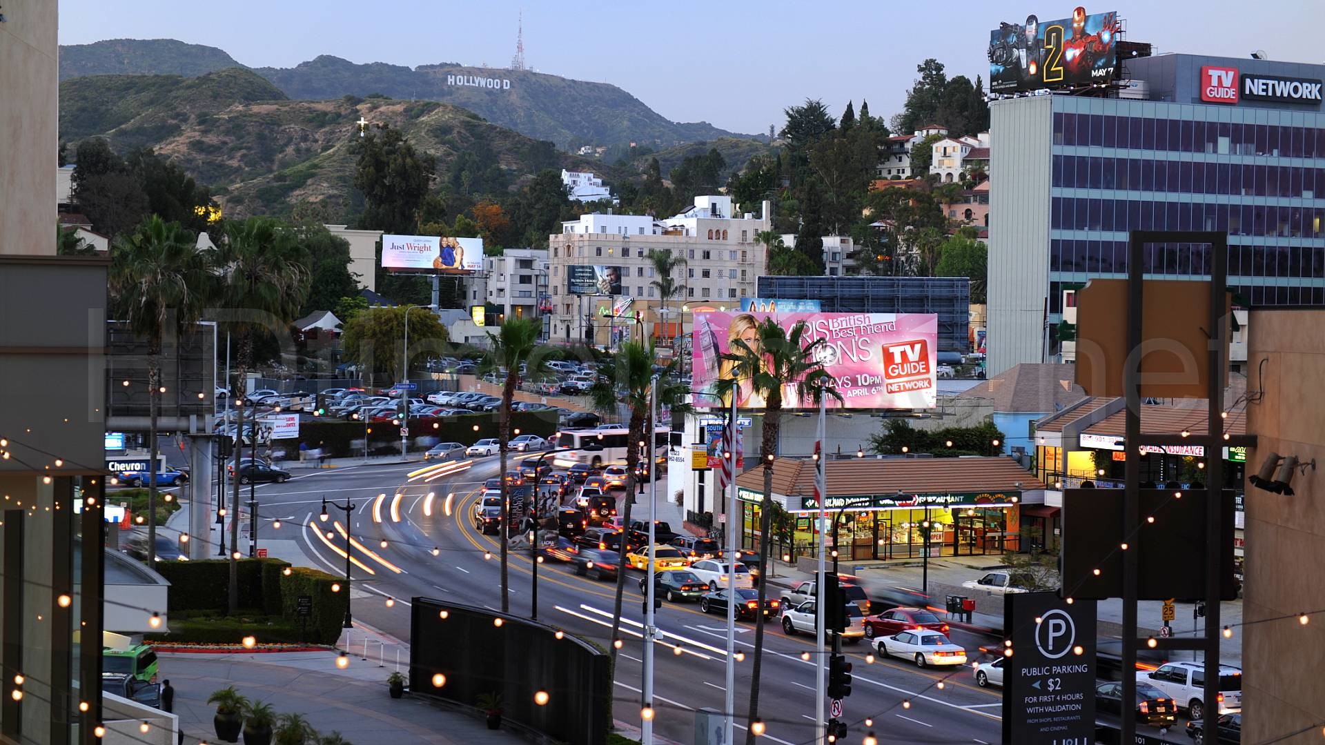 A vibrant dusk view of Hollywood, California, showcasing the iconic Hollywood Sign, bustling street traffic, and colorful billboards