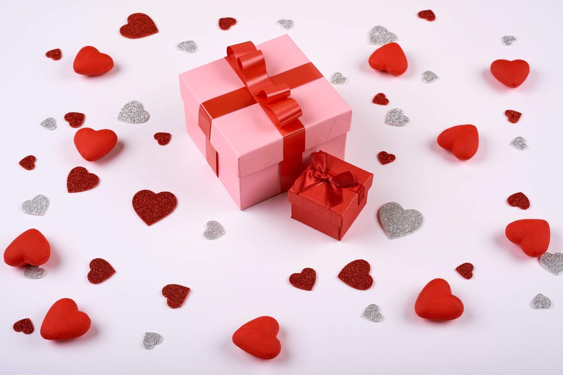 Two gift boxes and decorative hearts on a pink background create a festive Valentine's Day scene