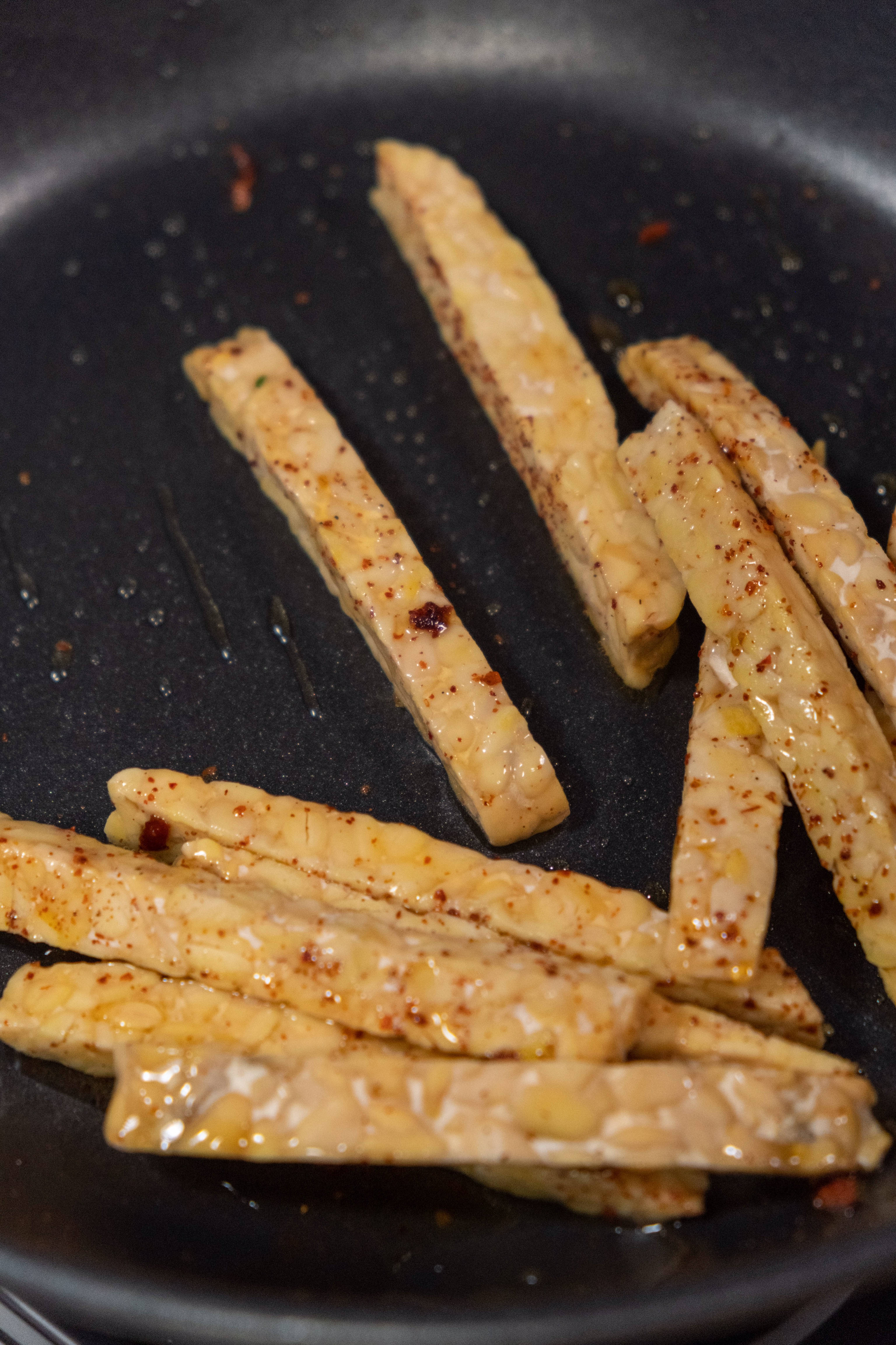 Close-up of tempeh strips cooking in a frying pan