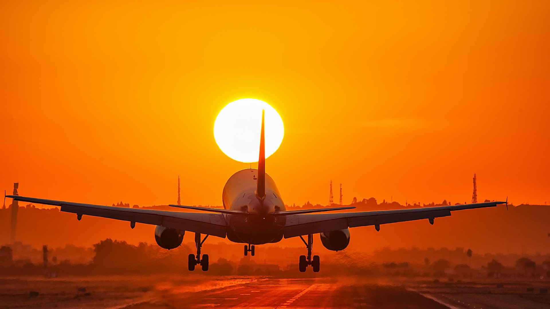 Silhouette of a passenger airplane landing against a vibrant orange sunset backdrop