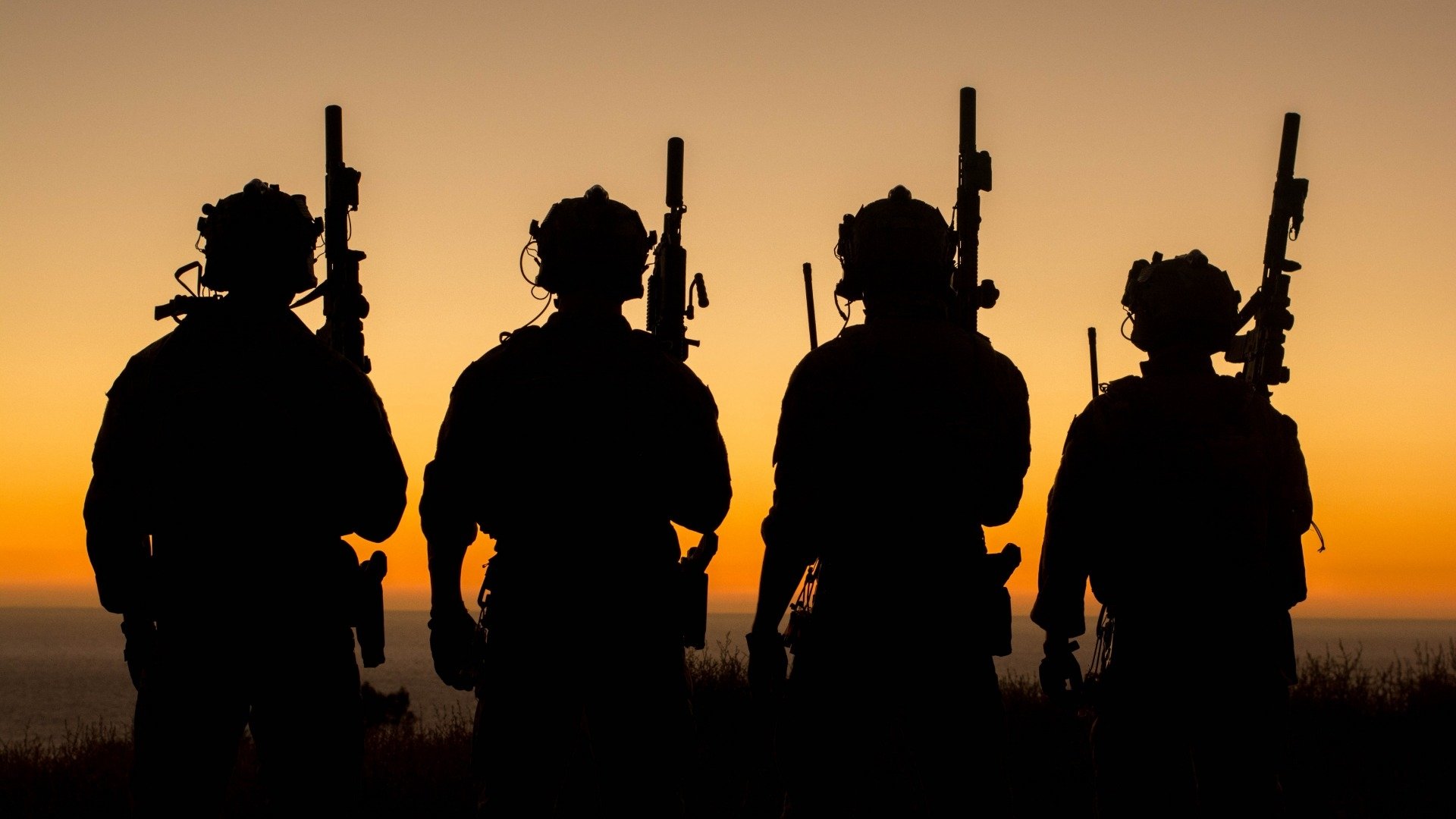 Silhouettes of four soldiers against a vibrant sunset, evoking a sense of duty and vigilance