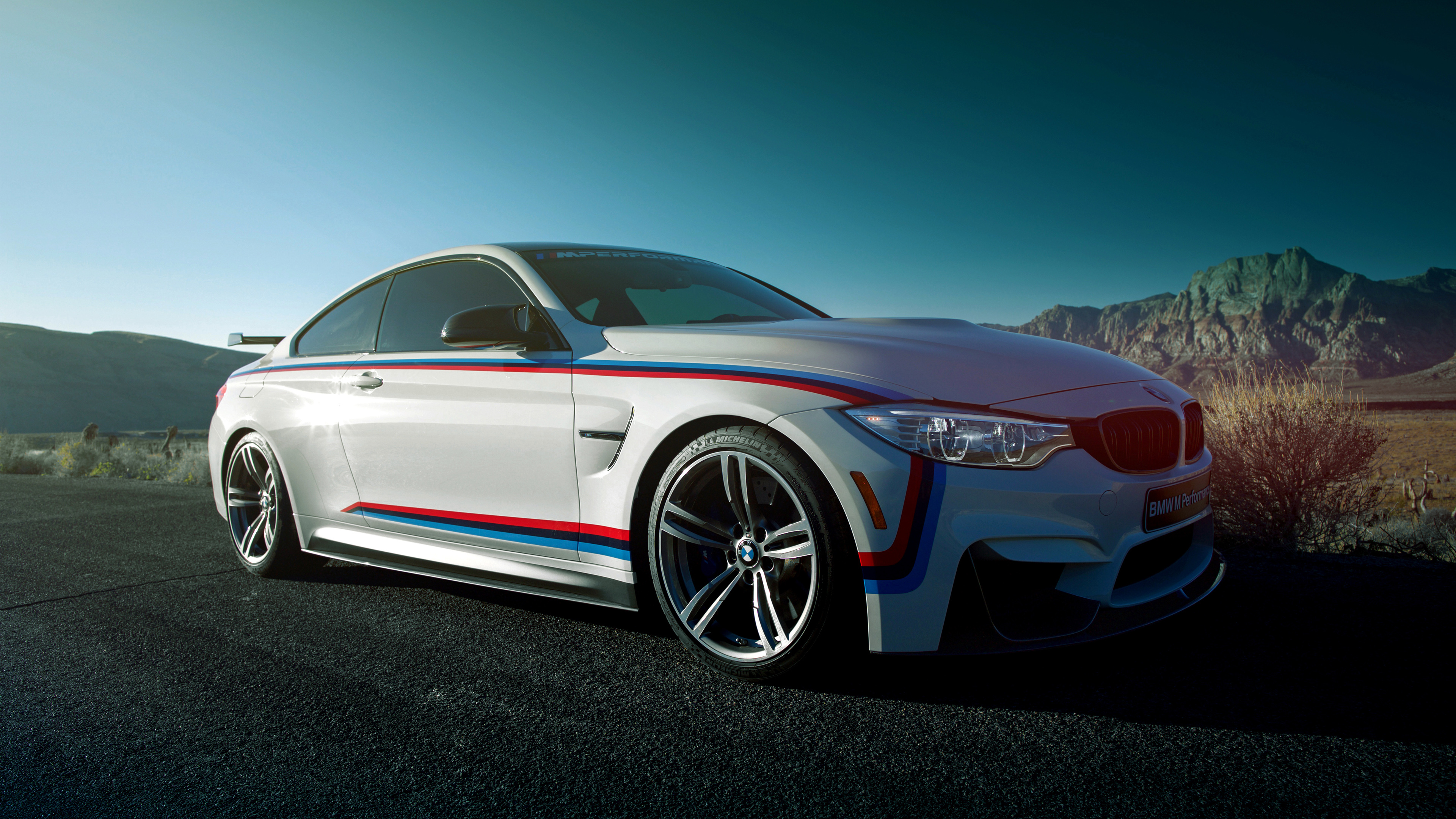 A white BMW M4 sports car parked on a desert road, showcasing its sleek design and motorsport-inspired livery