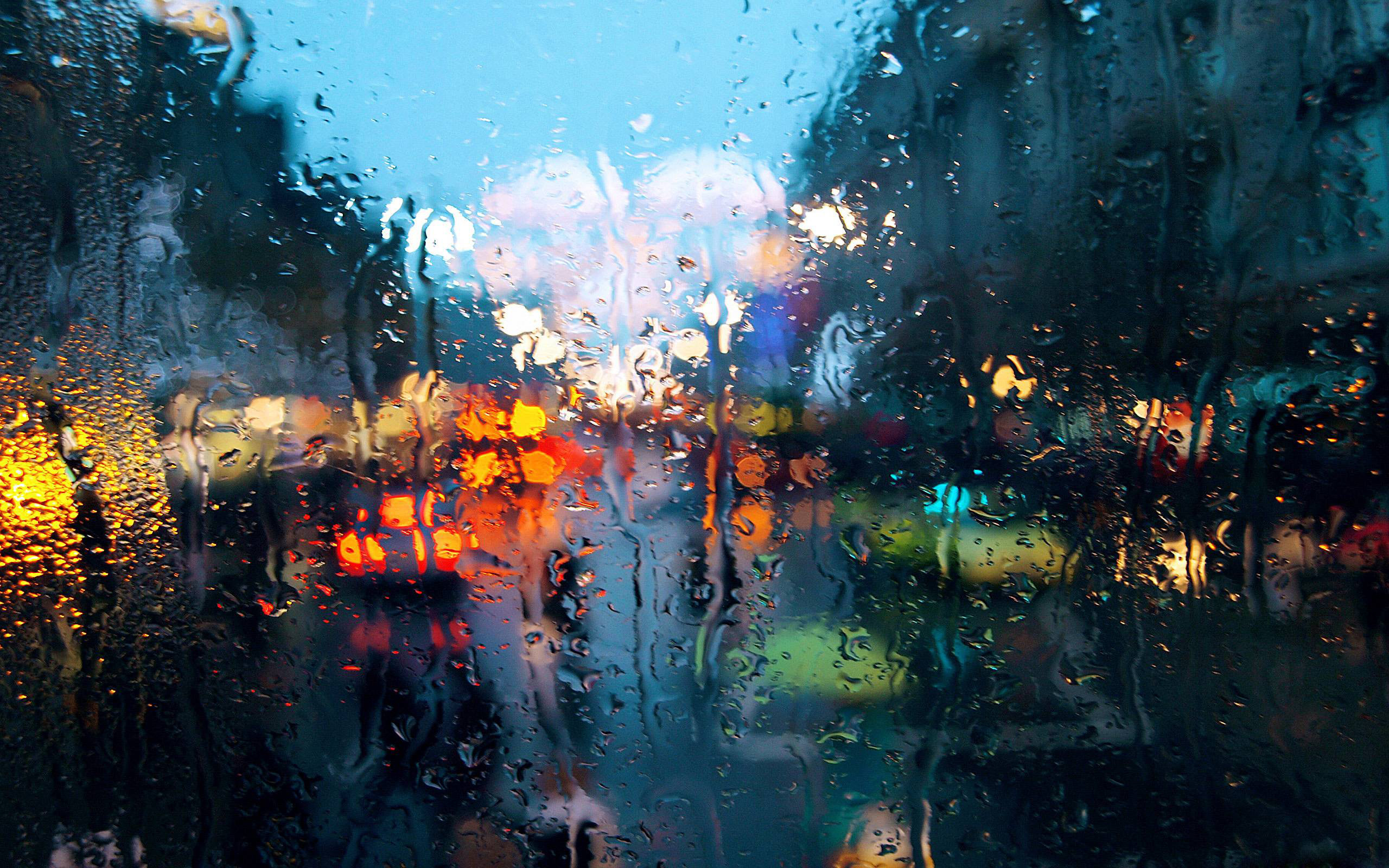 Raindrops on a window pane blur the city lights in a rainy night scene