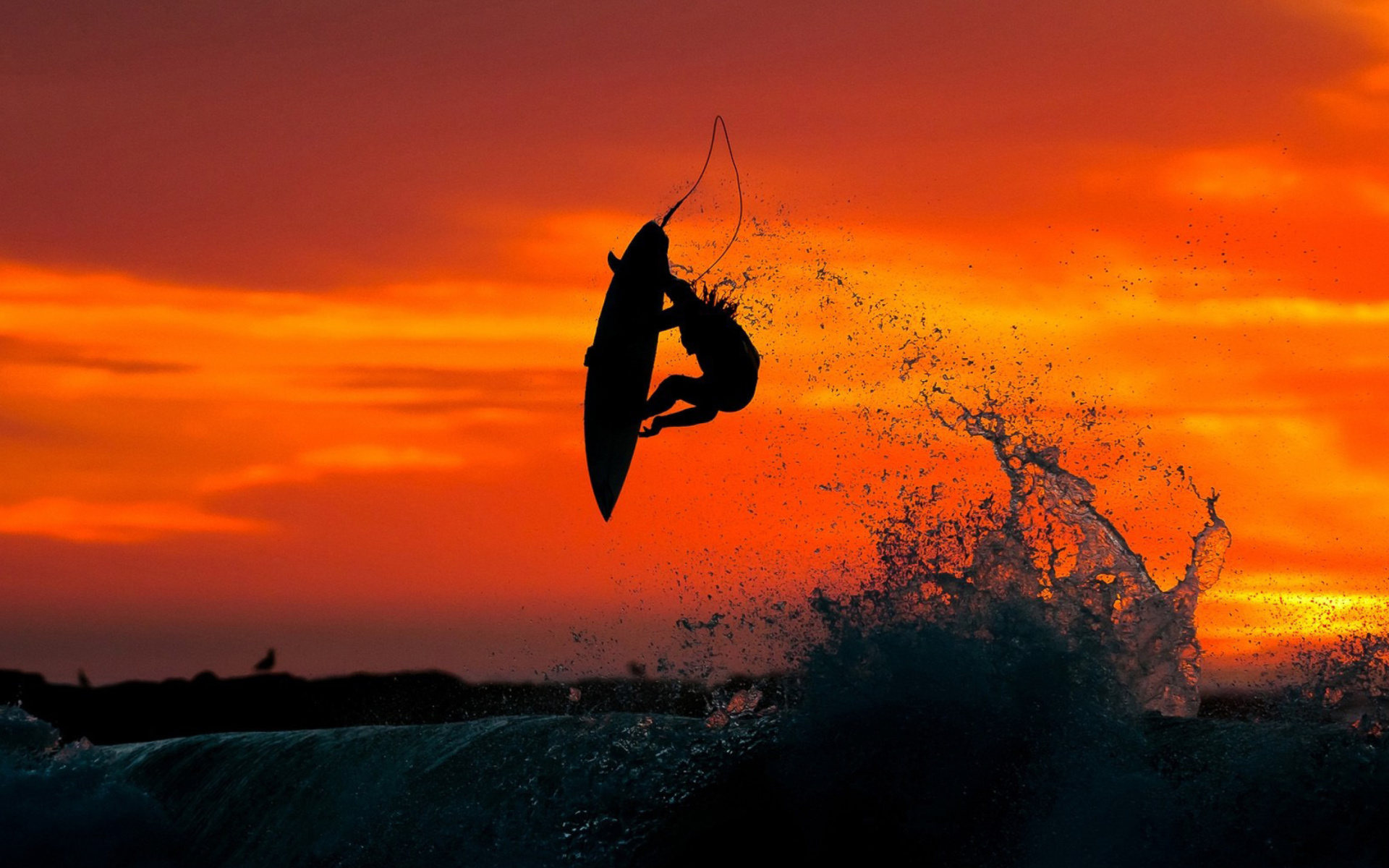 Silhouette of a surfer performing an aerial maneuver against a vibrant sunset backdrop