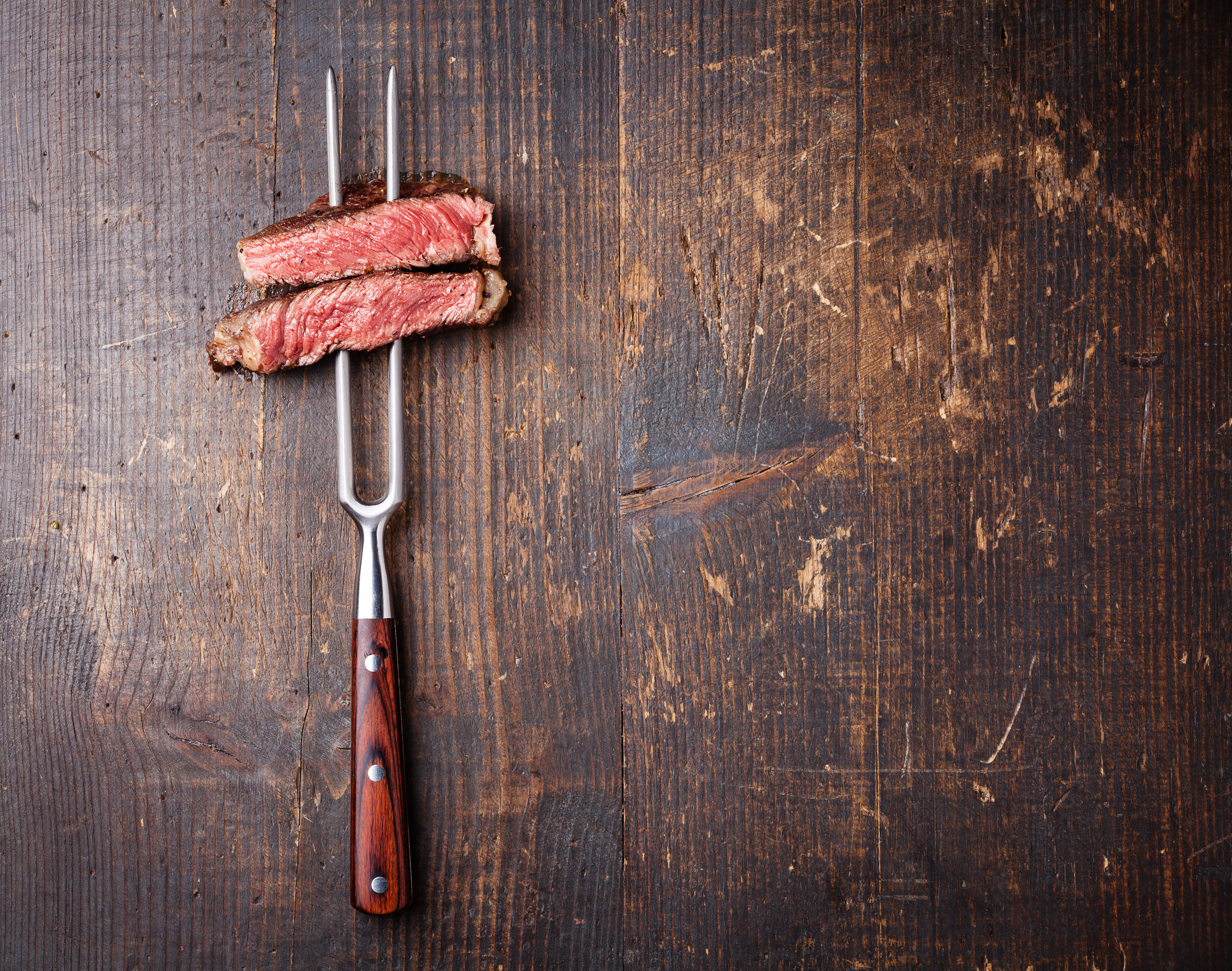 Slices Of Beef Steak On Meat Fork Dark Wooden Background
