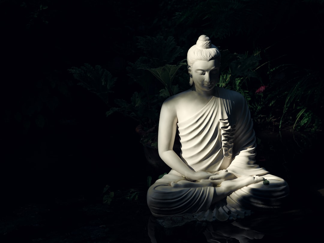 Serene white Buddha statue meditating peacefully in a dark, lush garden