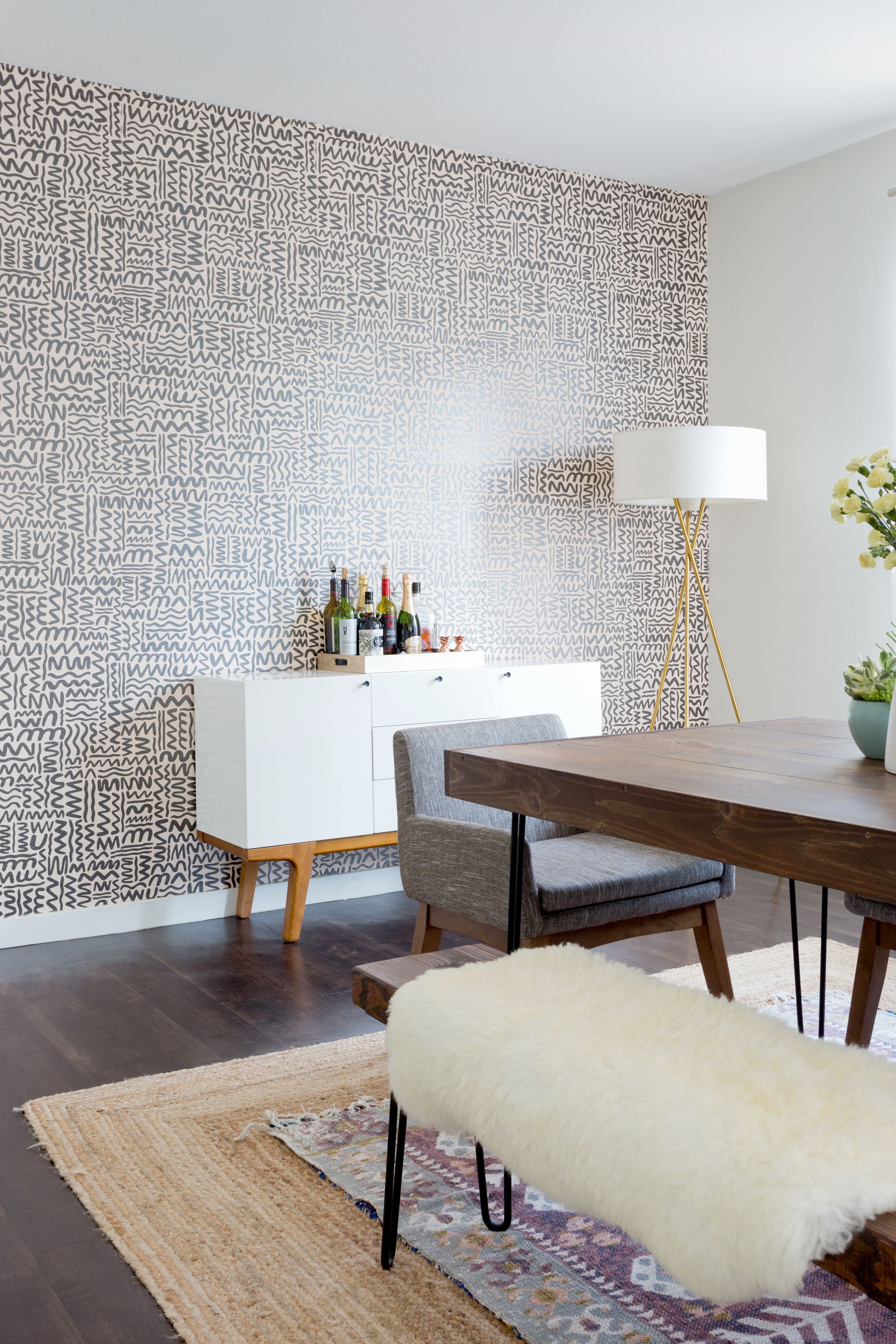 A dining room with a wallpaper accent wall and layered rugs