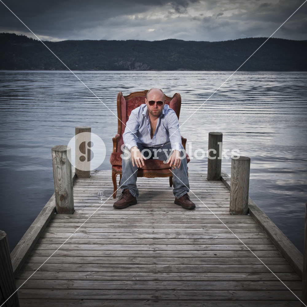Sleazy Man In A Classic Vintage Chair On Pier With Water And Sky