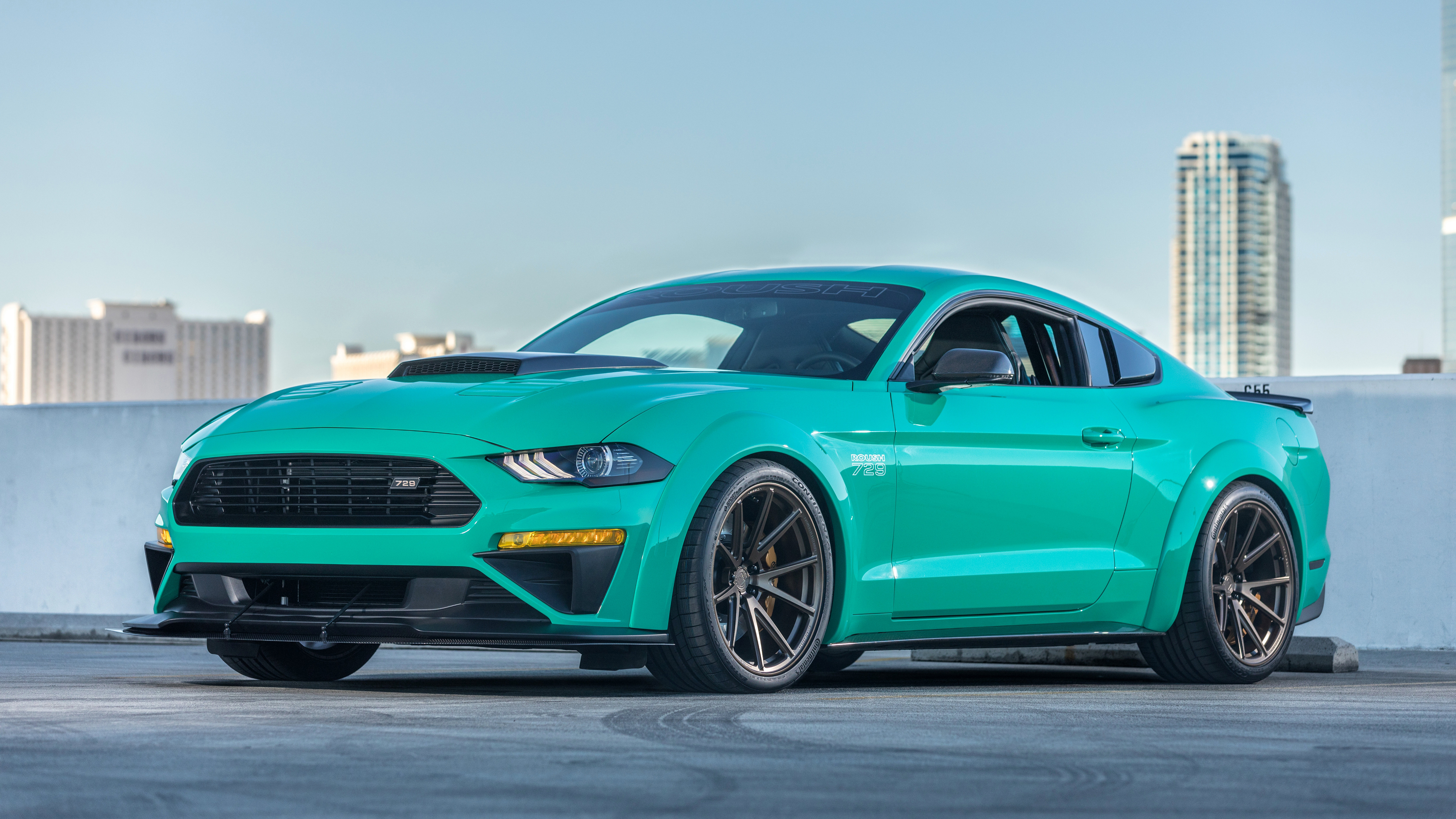 Teal Ford Mustang parked in front of a city skyline